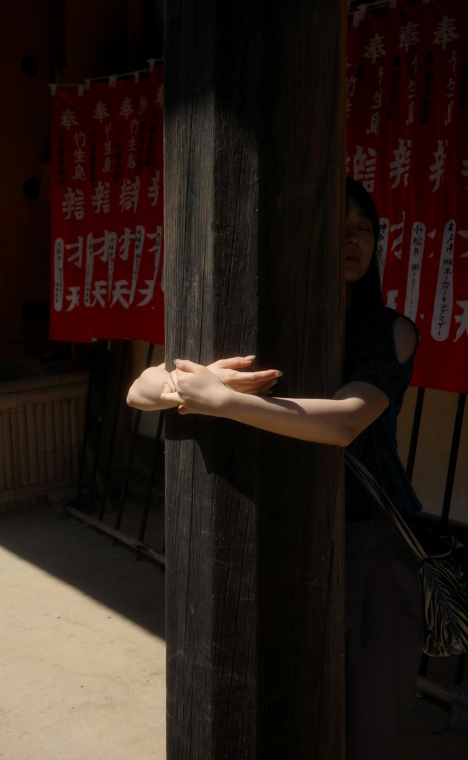 女性的手臂環抱木柱，背景有紅色橫幅