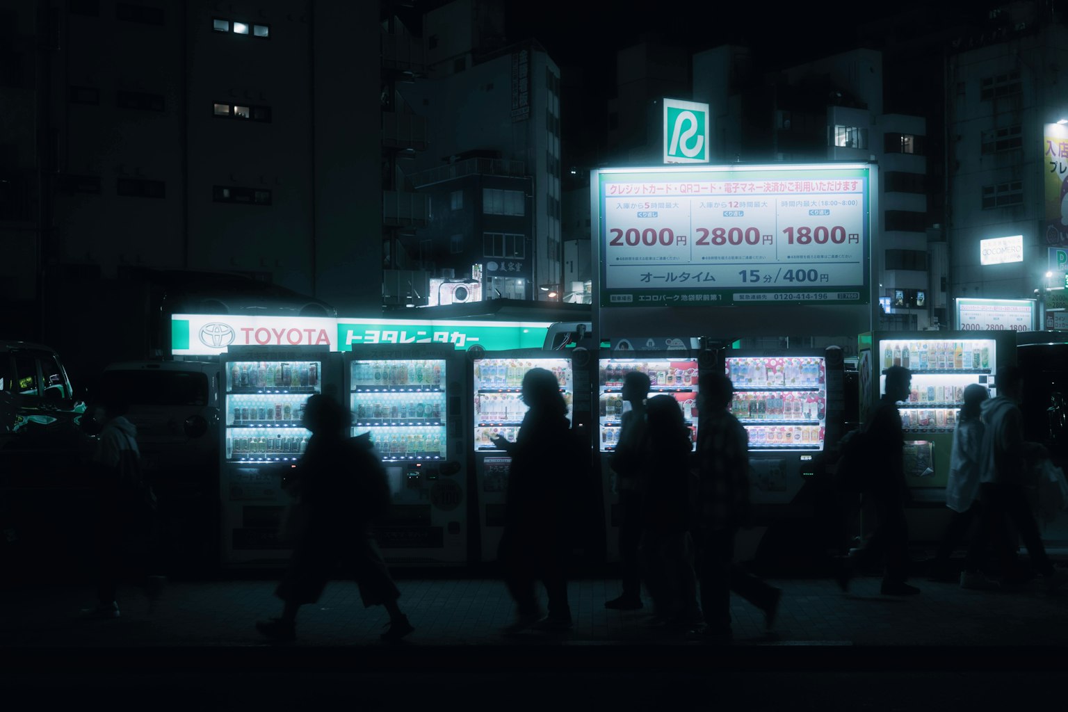 Silhouette di persone che camminano in una strada buia con distributori automatici illuminati