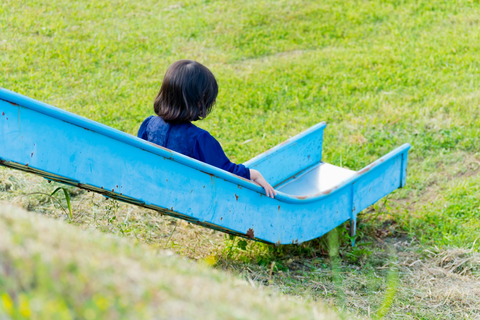 Anak duduk di perosotan biru di atas rumput hijau