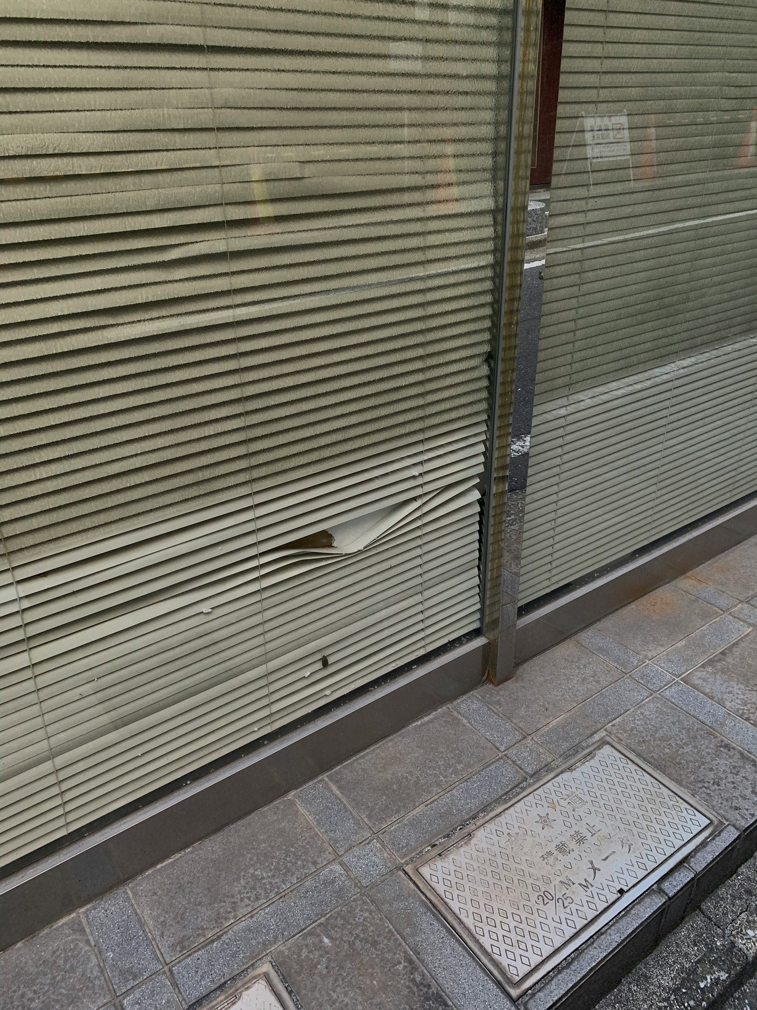 Sección dañada cerca de la ventana de una tienda cerrada con persianas