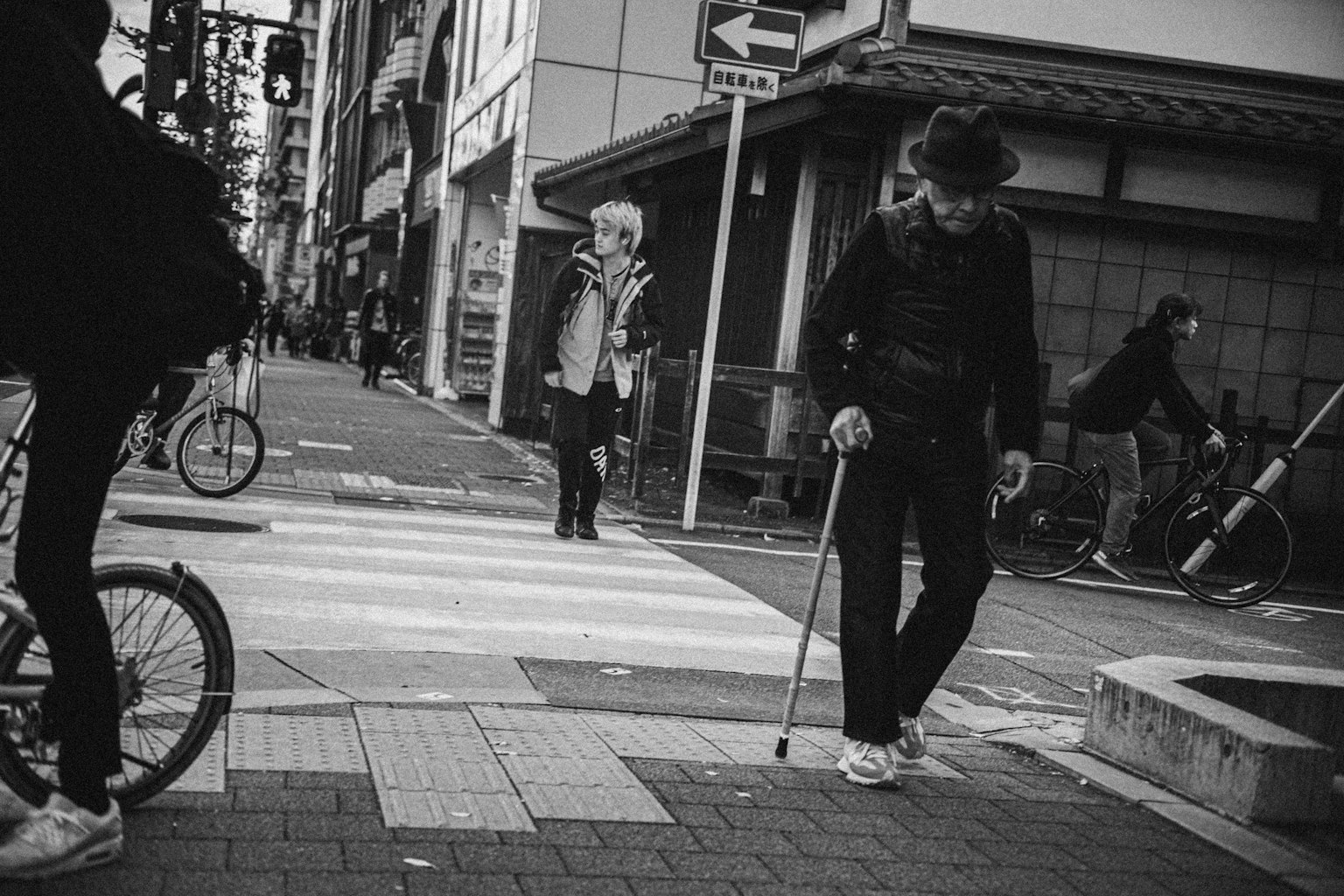 白黒の街角で横断歩道を渡る人々と自転車が見える