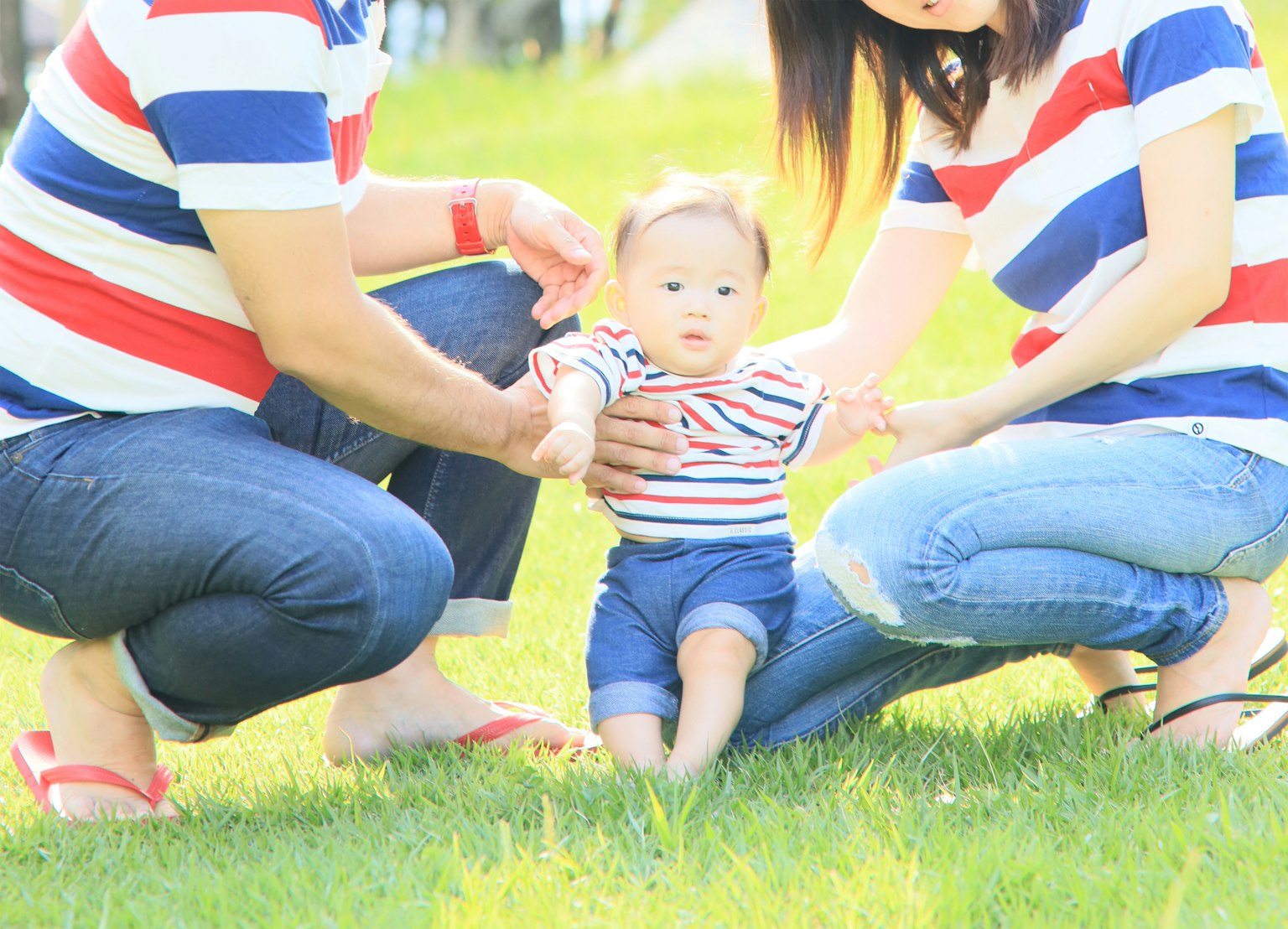 Family supporting a baby in striped shirts on green grass