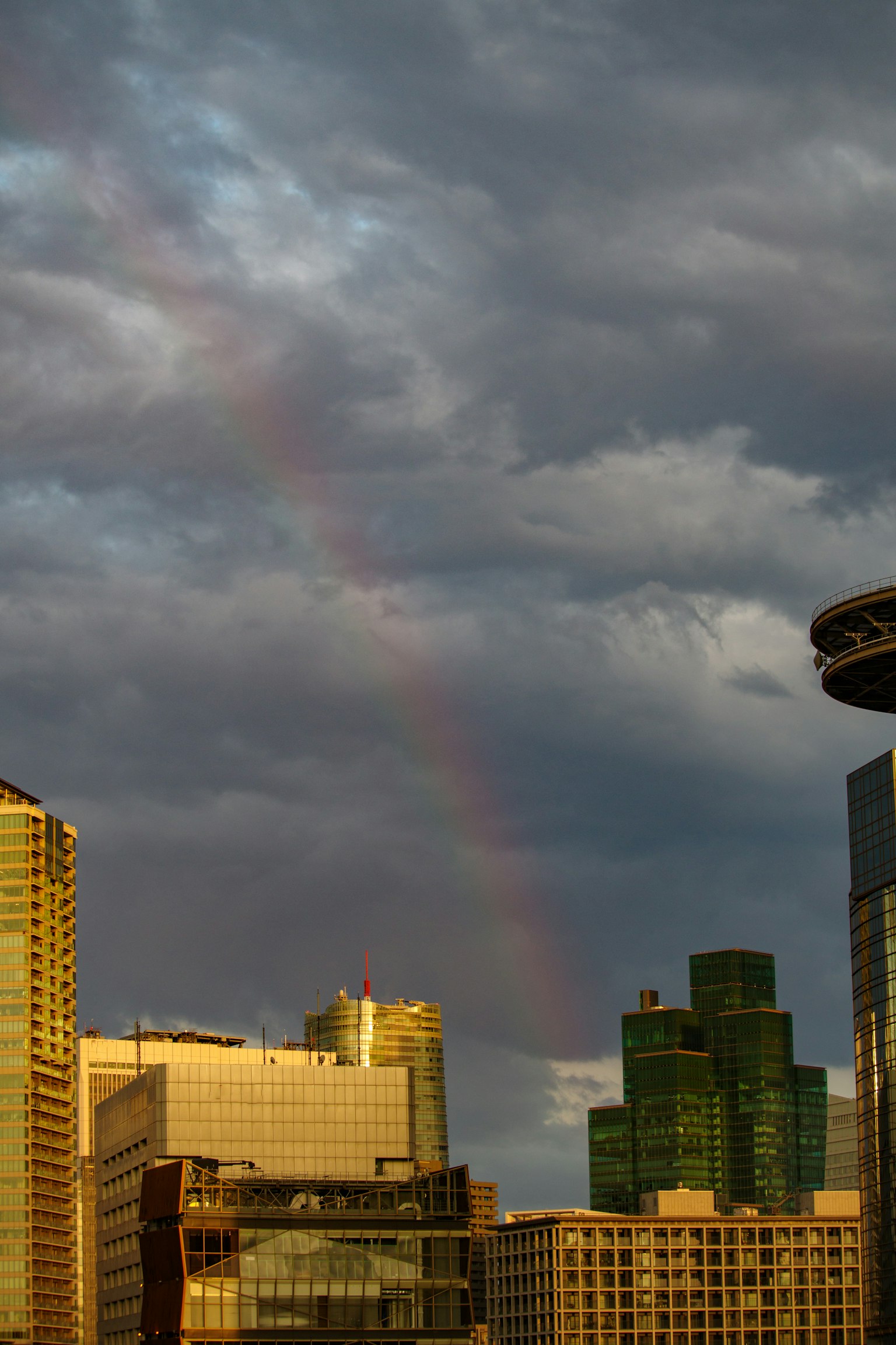 Stadtansicht mit Wolkenkratzern unter dunklen Wolken und einem Regenbogen