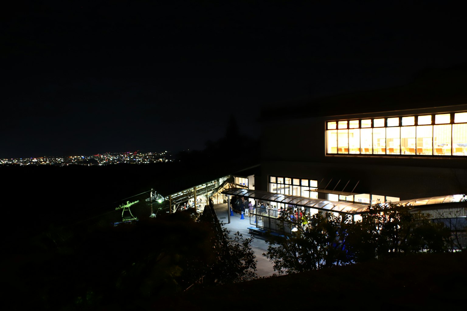 Vista exterior de un edificio iluminado por la noche con un paisaje urbano de fondo