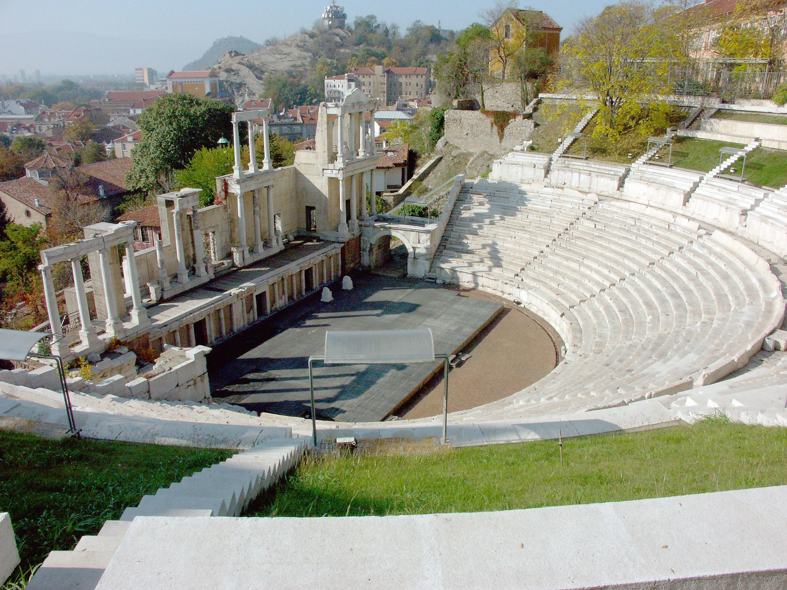 Ancient theater view featuring stone seating and remaining columns surrounded by greenery