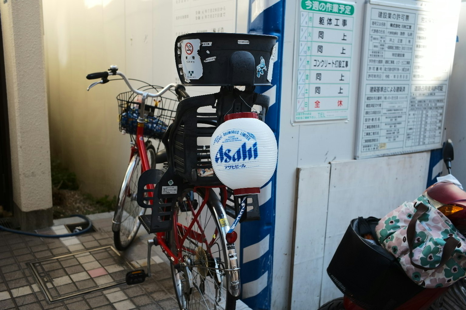 Bicicletta rossa appoggiata a un muro con logo Asahi nel cestino