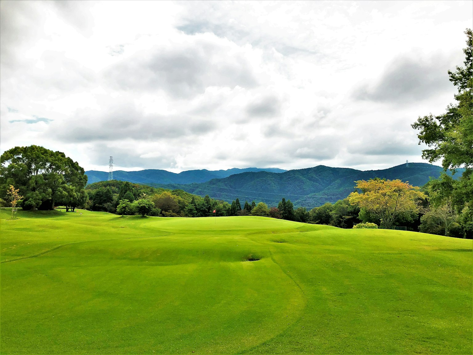 Lush green golf course with rolling hills and mountains in the background