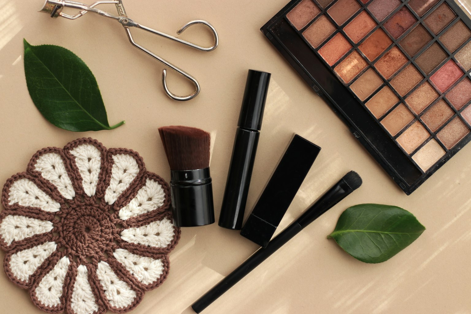 Vue de dessus de cosmétiques et d'outils avec une palette de maquillage et un pinceau accompagnés de feuilles vertes et d'une nappe en dentelle