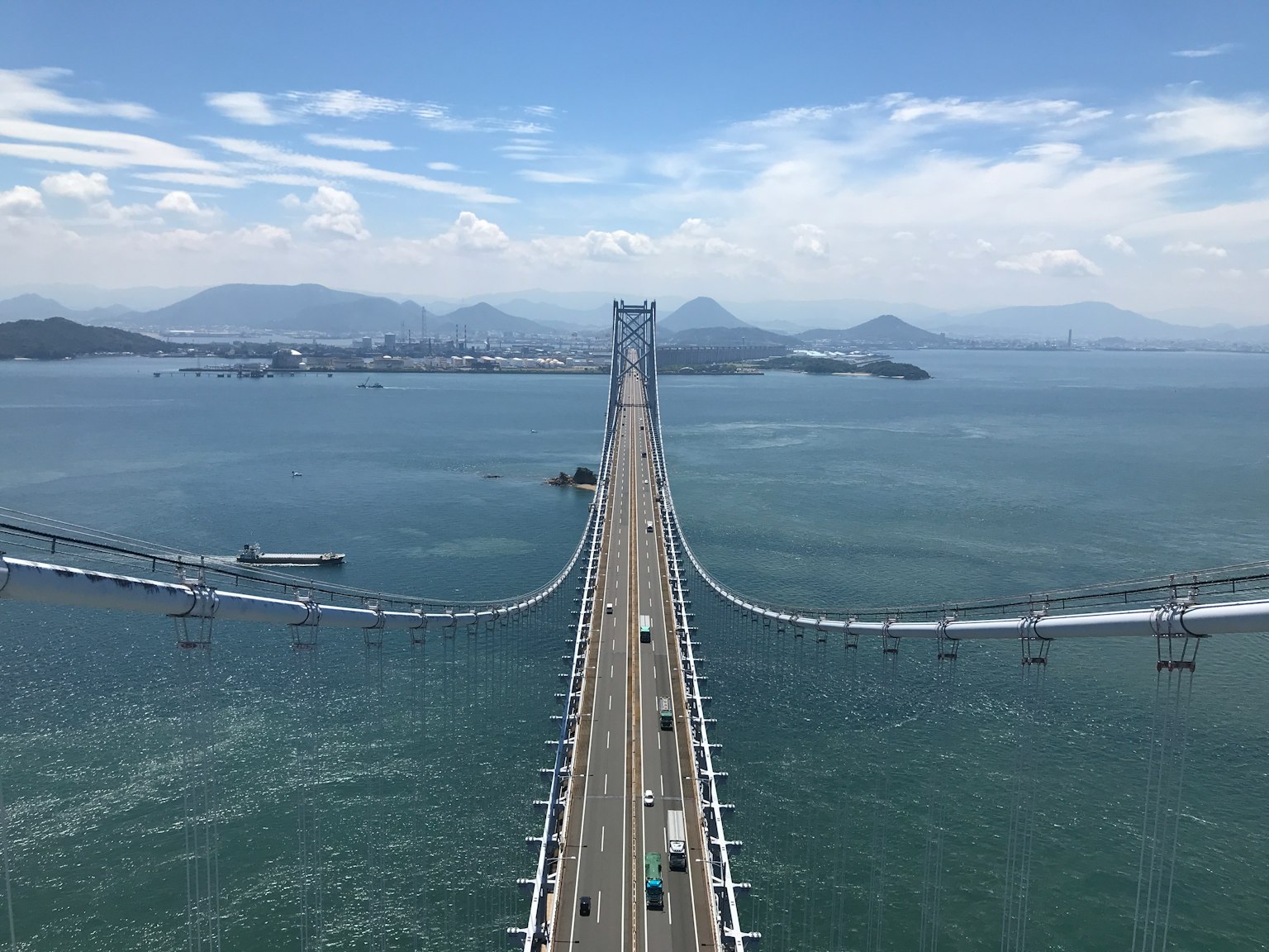 Jembatan panjang membentang di atas air biru di bawah langit cerah