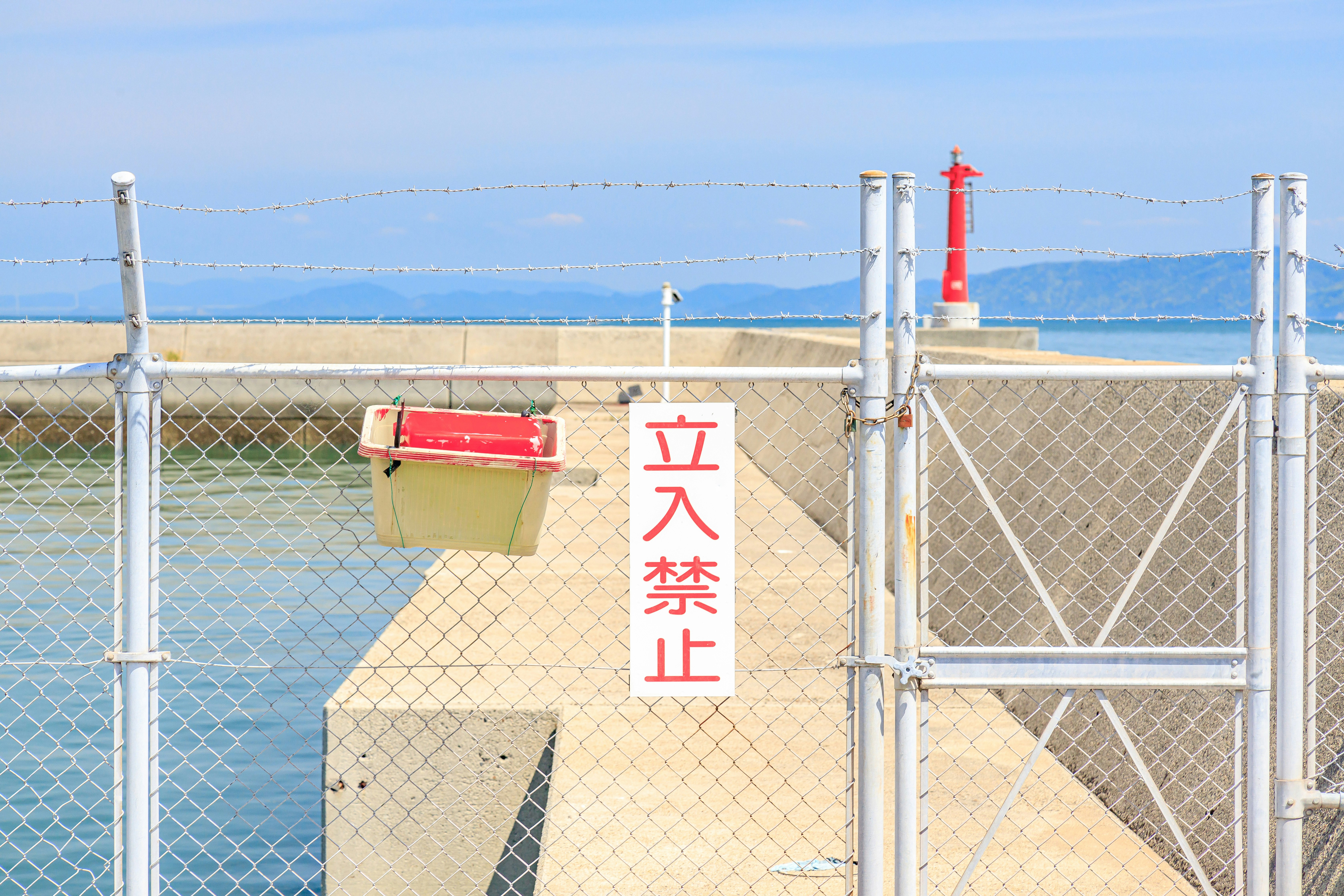 青空の下の防波堤フェンスと灯台