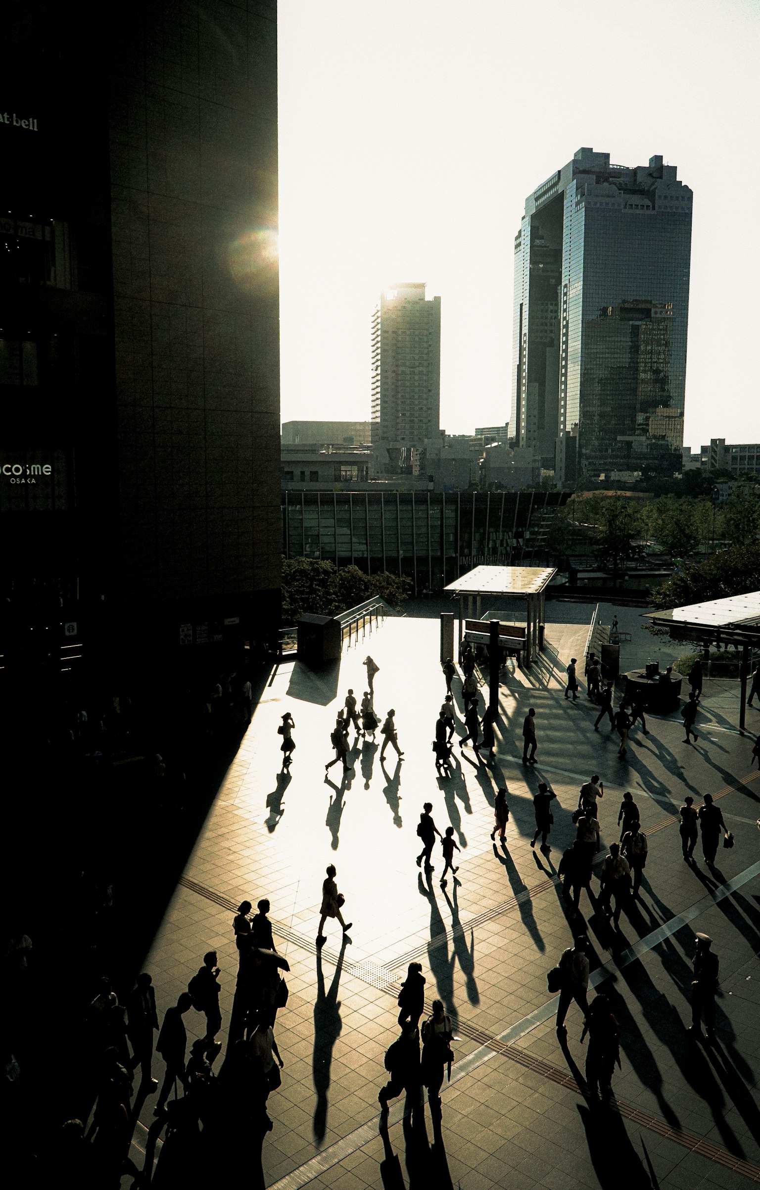 Escena urbana con personas caminando y sombras largas durante el atardecer