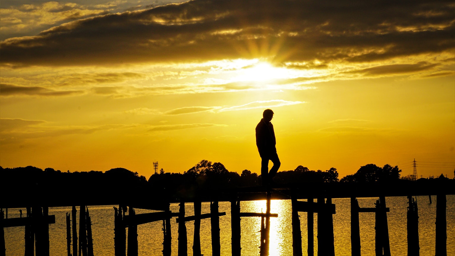 Silueta de una persona de pie en un muelle contra un atardecer