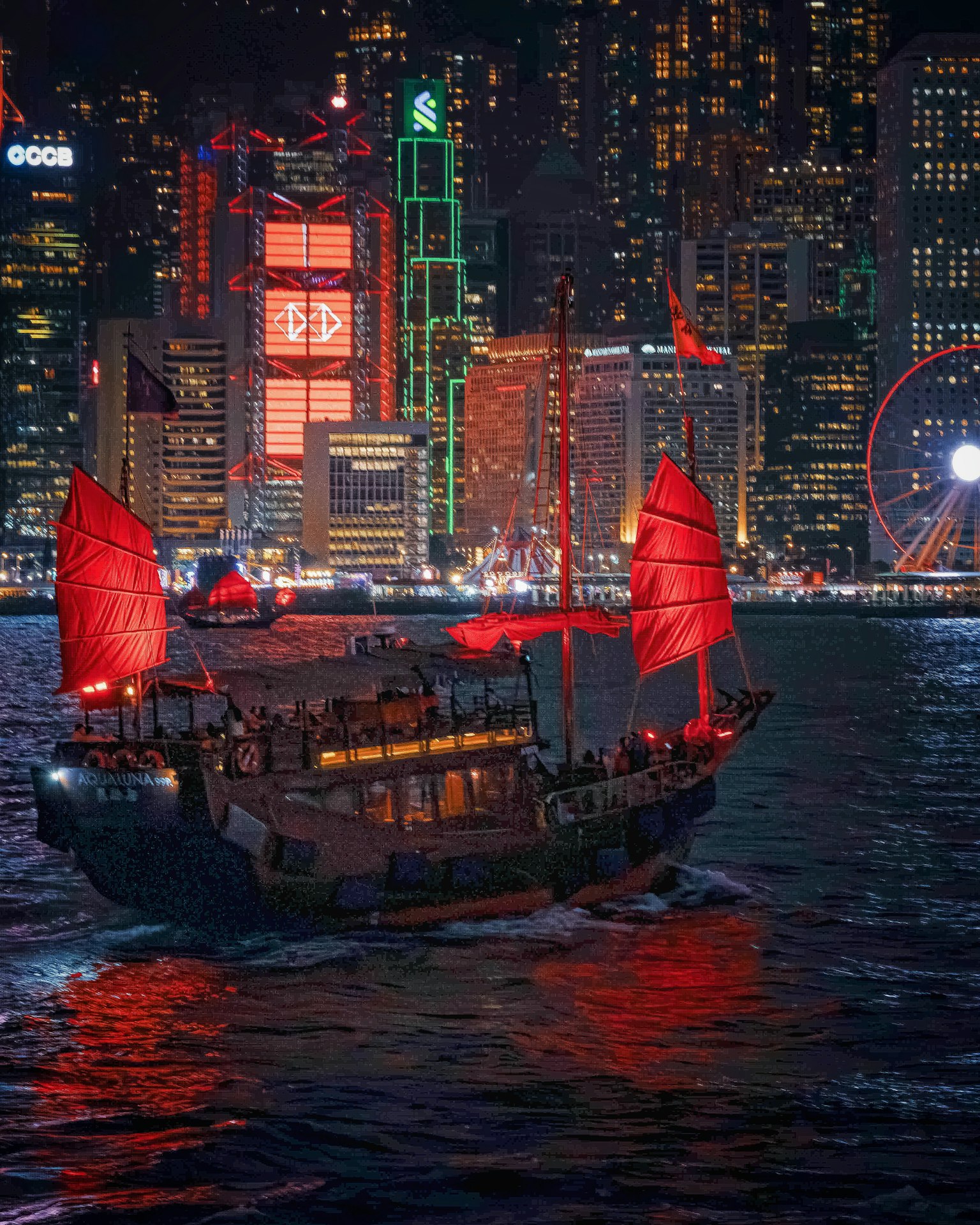 夜晚在香港港口航行的紅帆船與照亮的摩天大樓