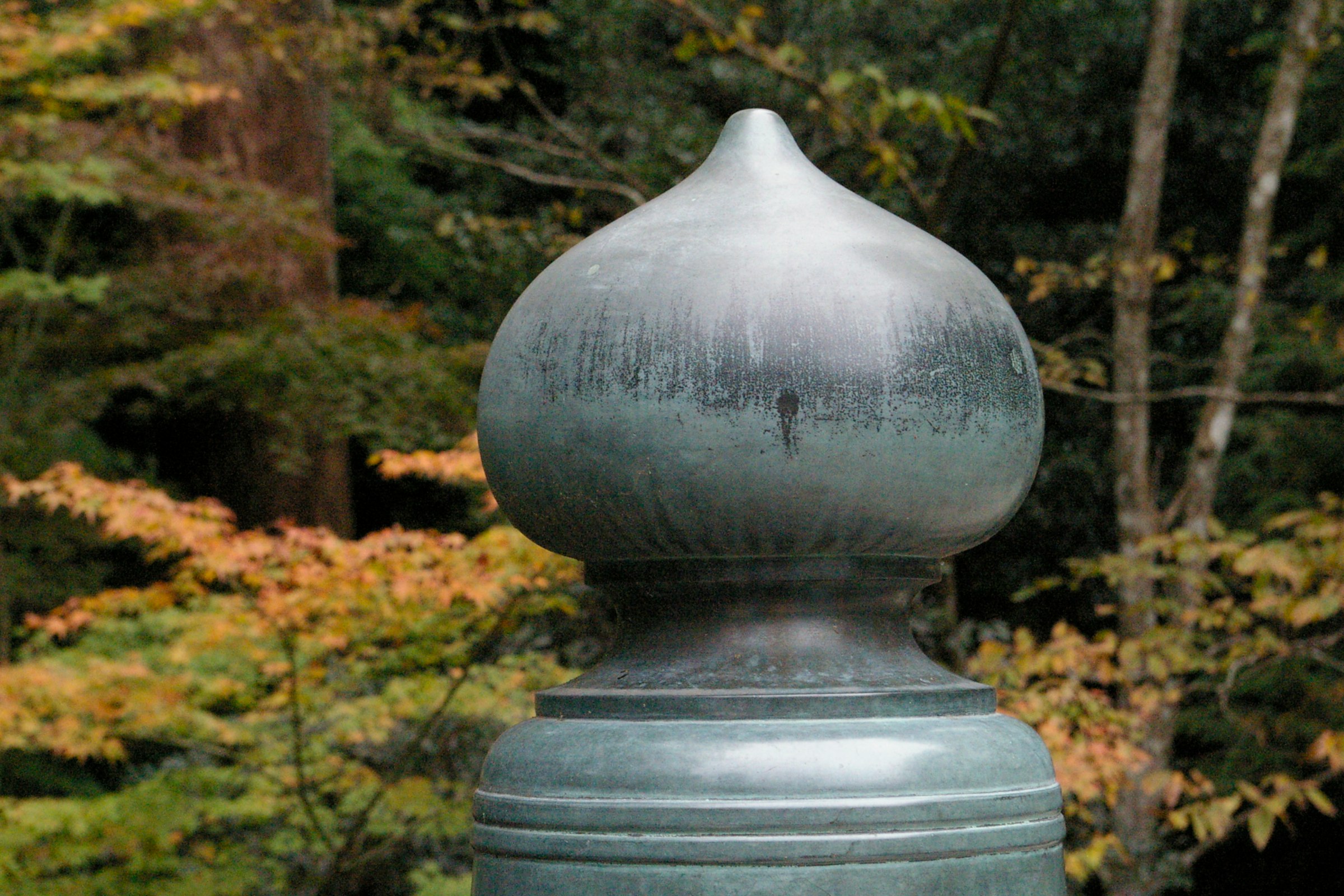runder Metall-Buddhaaufsatz auf steinernem Sockel im Garten
