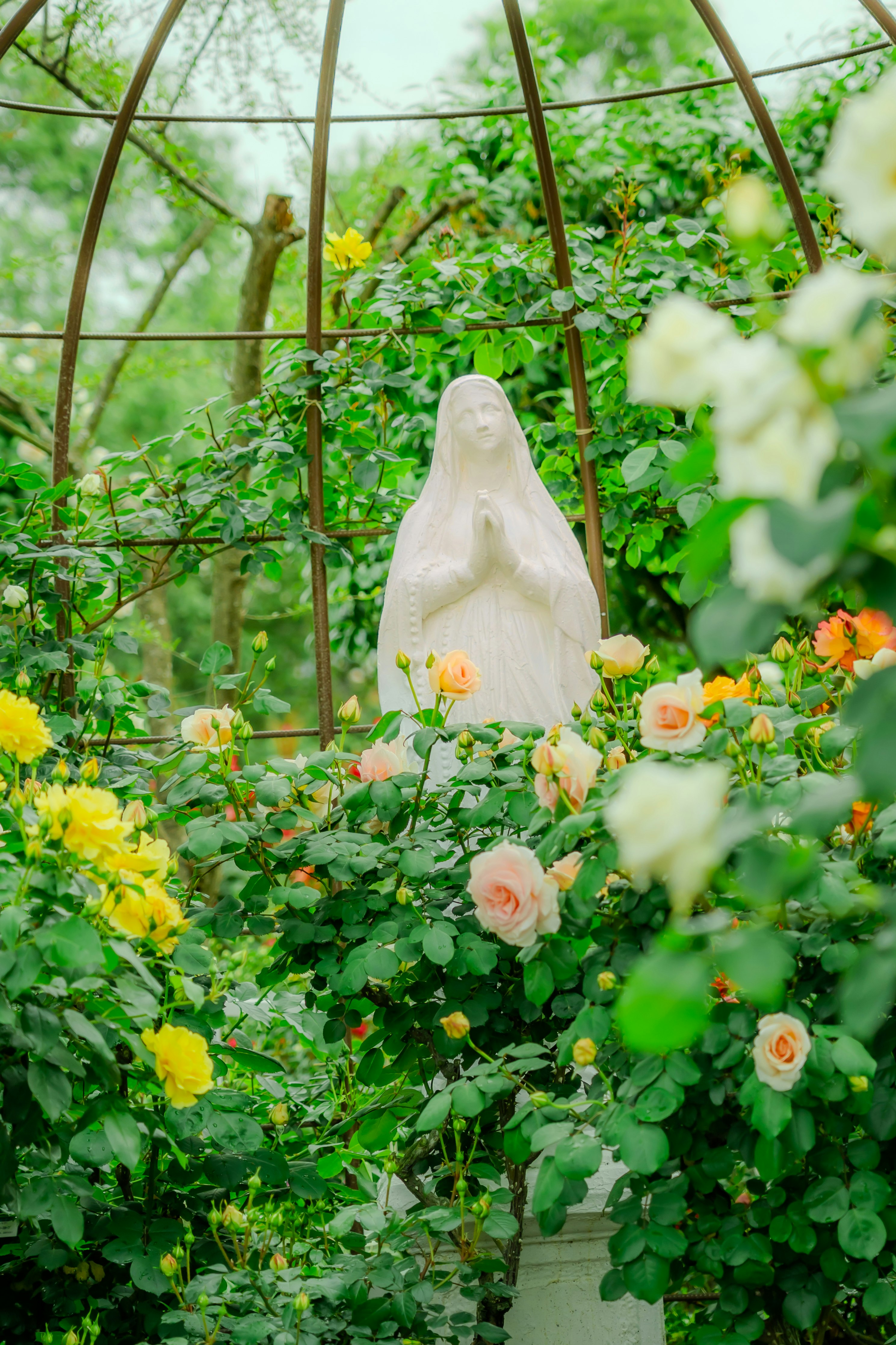 garden arch with a stone statue surrounded by flowers in a lush green garden