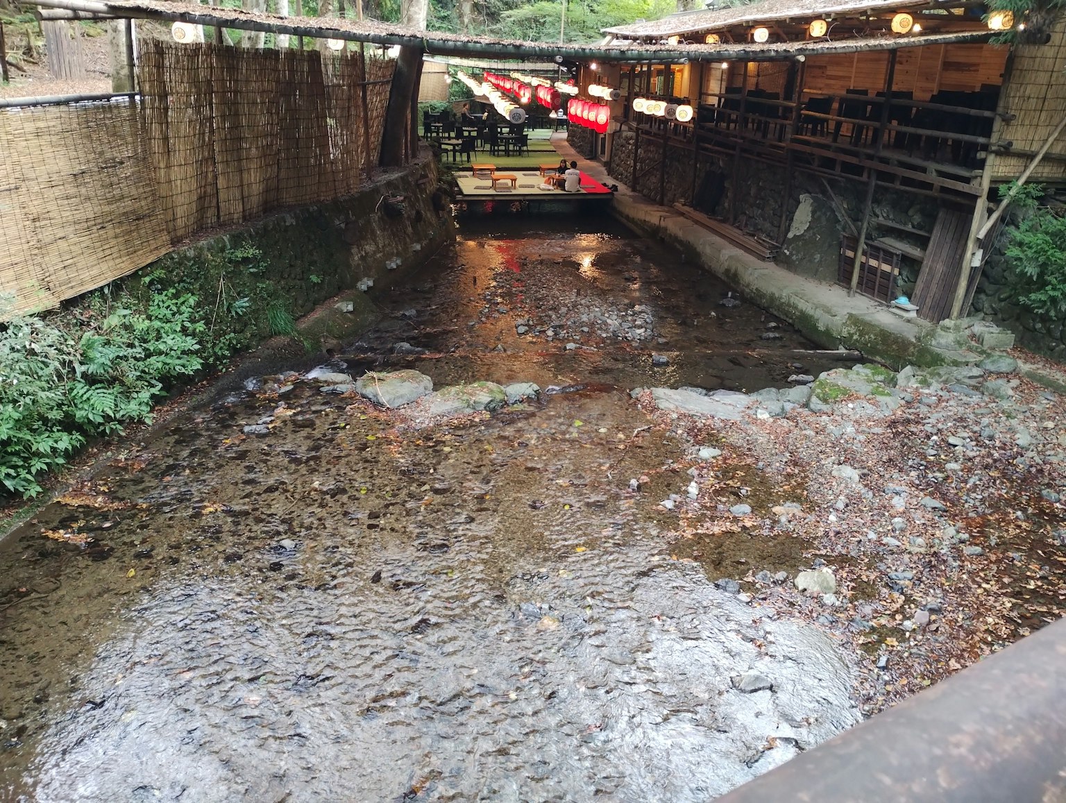 Aliran sungai dengan vegetasi subur dan area istirahat yang tertutup terlihat