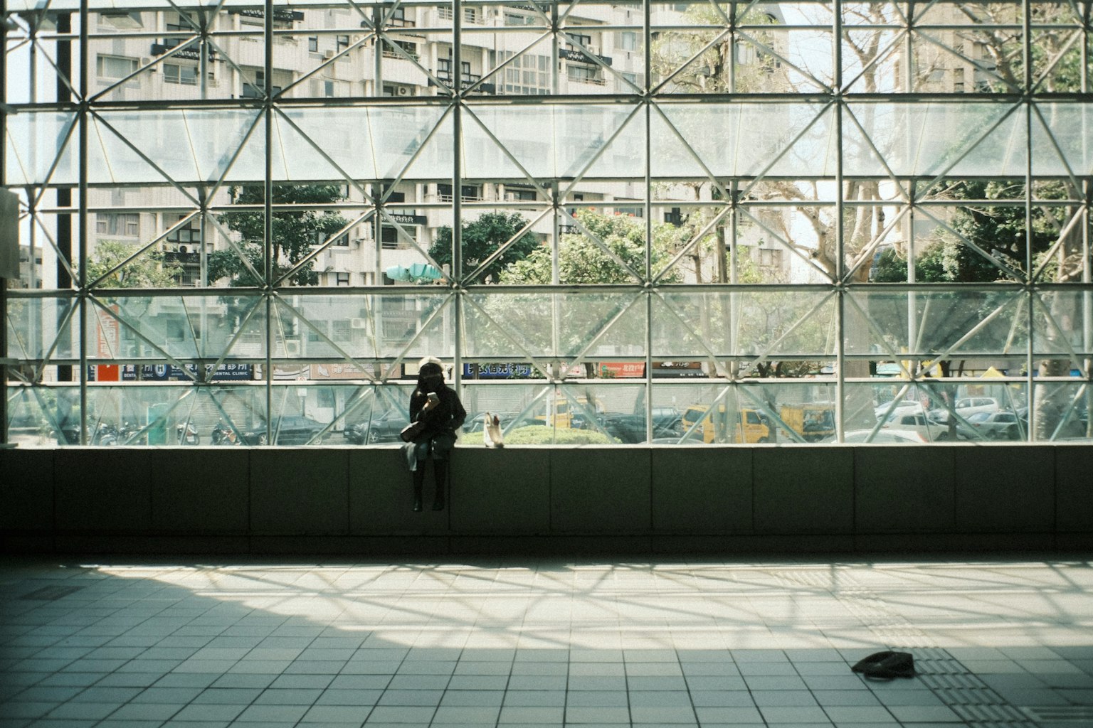 坐在现代建筑墙壁上的女性，窗户很大