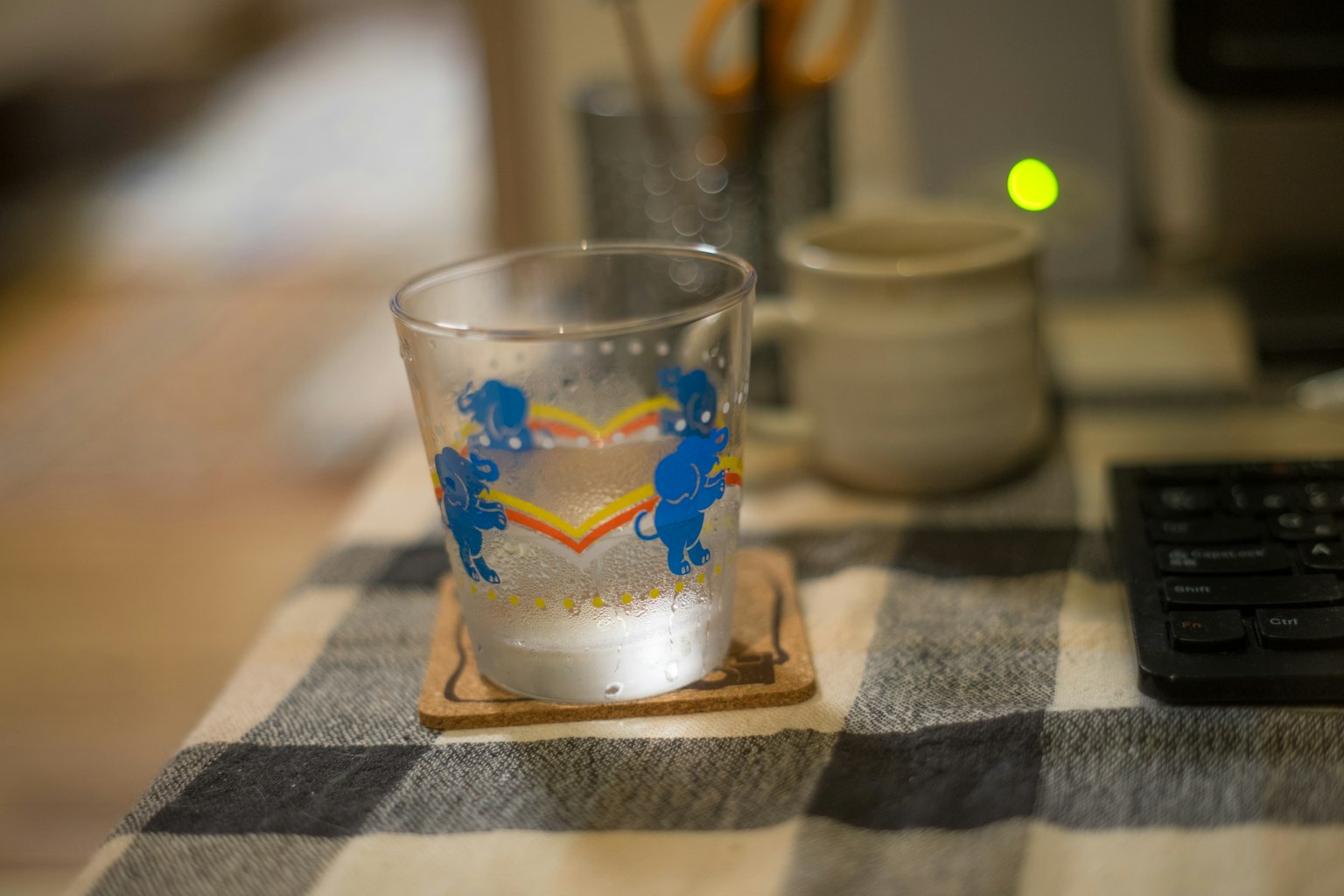 一只透明的玻璃杯，上面有蓝色角色插图，装着饮料，放在桌子上