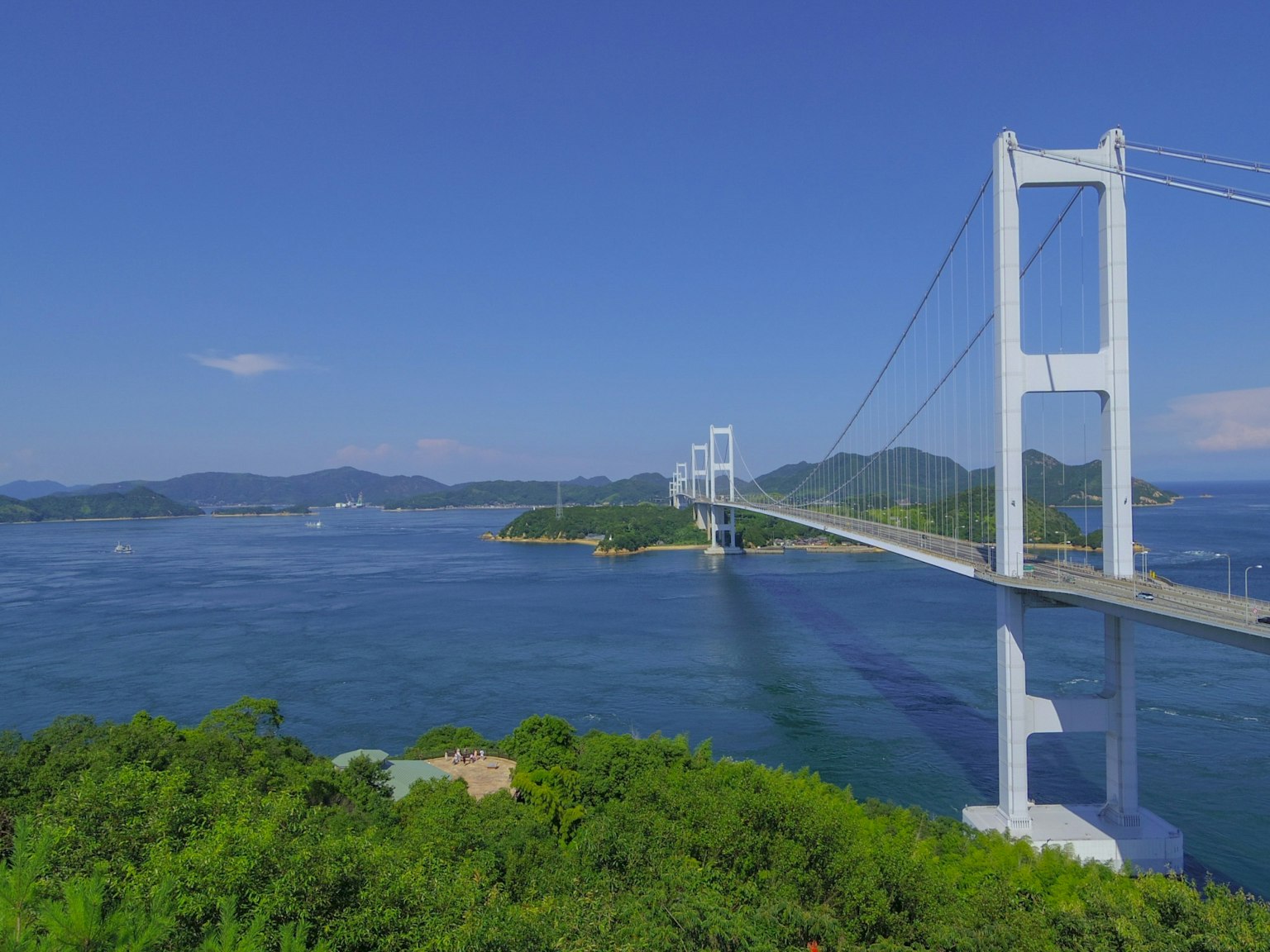 Eine schöne Brücke, die über blaues Wasser unter einem klaren Himmel mit üppigen grünen Inseln in der Nähe spannt