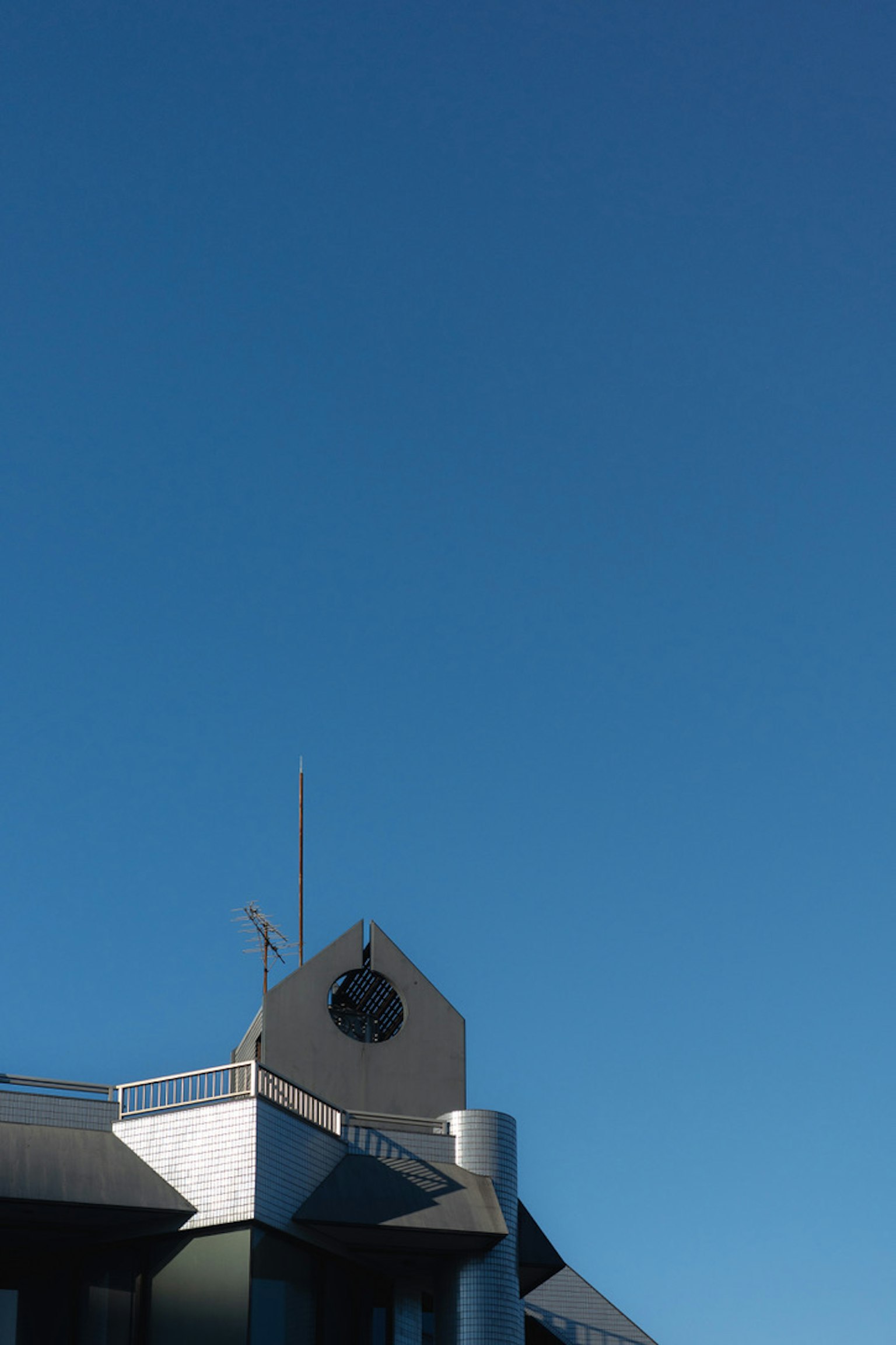 Parte di un edificio moderno sotto un cielo blu con un simbolo visibile sul tetto