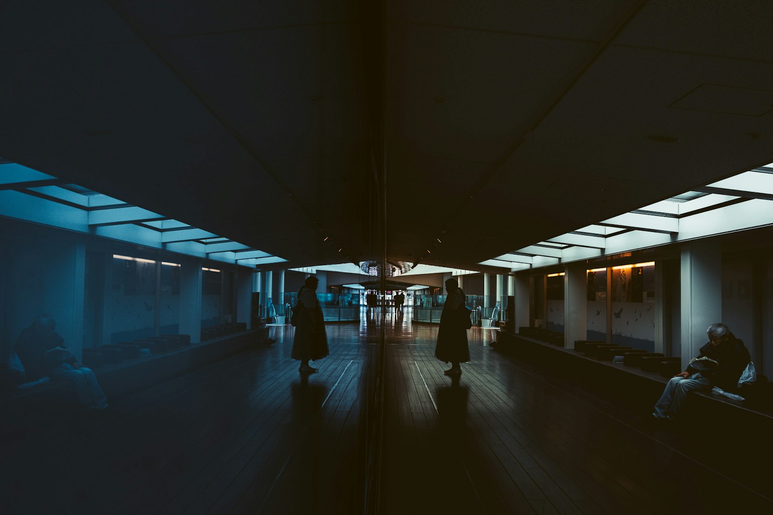 Corridoio debolmente illuminato con persone che camminano caratterizzato da luce blu e riflessi