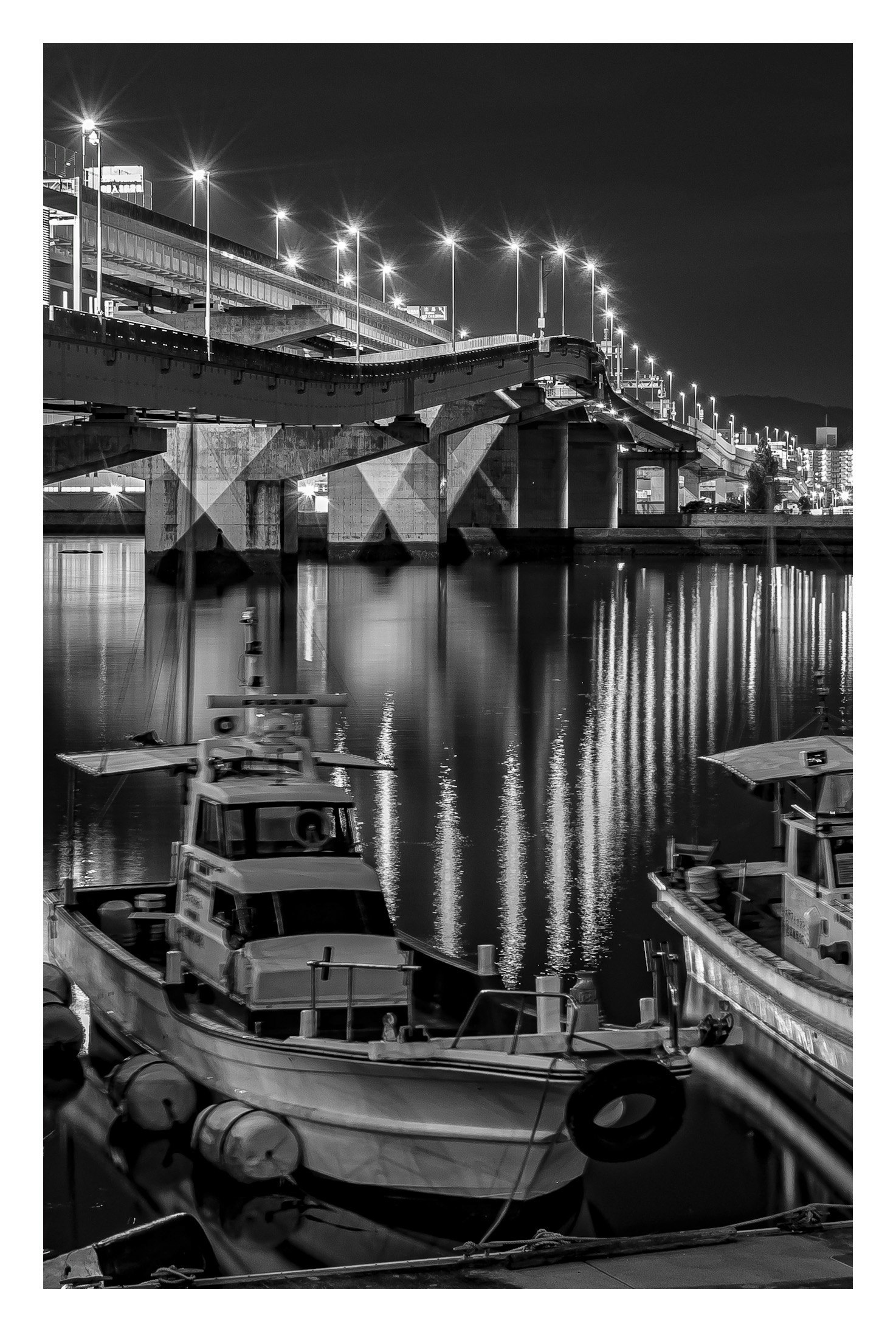 モノクロの港で並ぶボートと高速道路の高架の夜景
