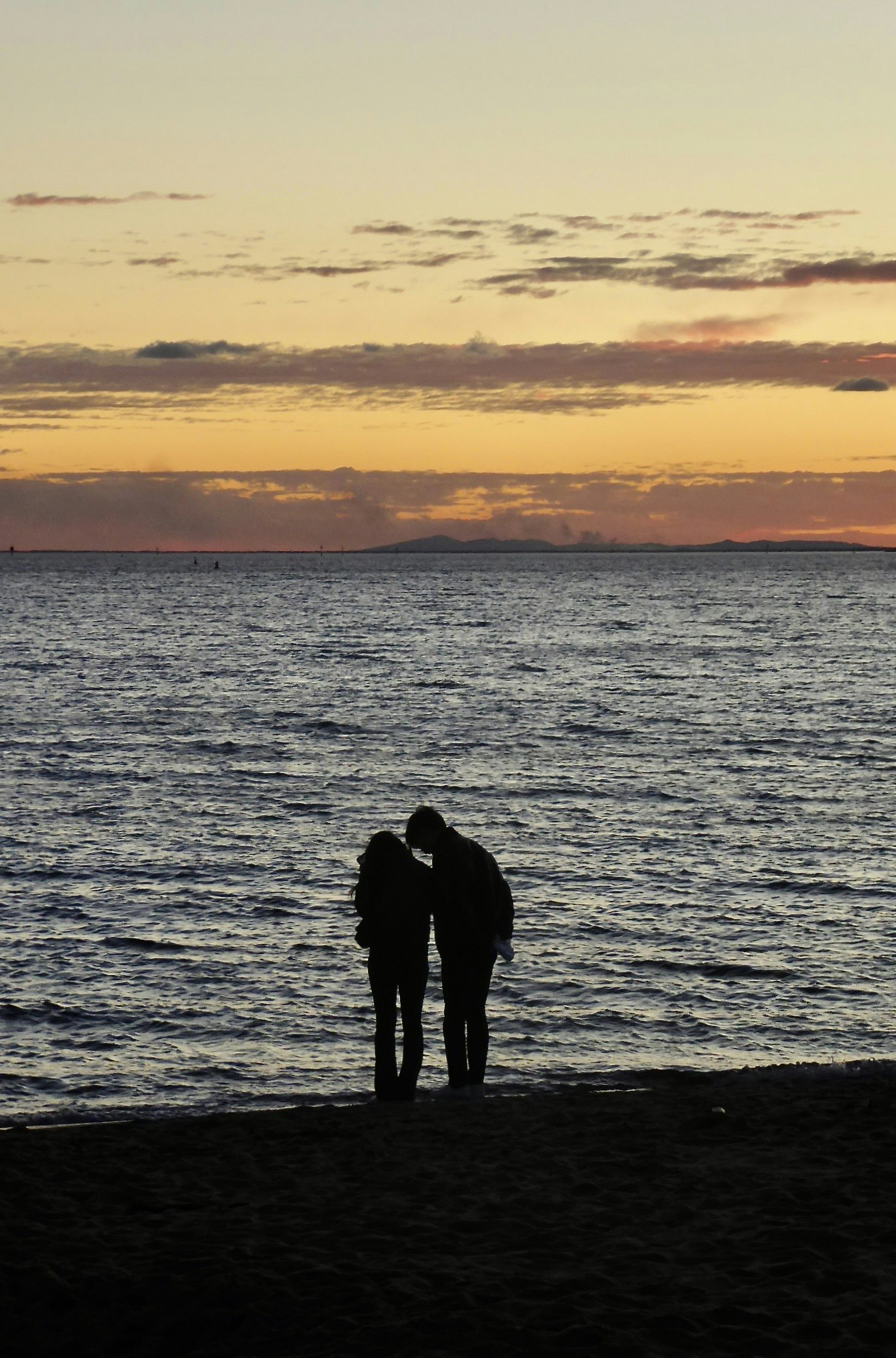 夕暮れの海辺で寄り添うシルエットのカップル