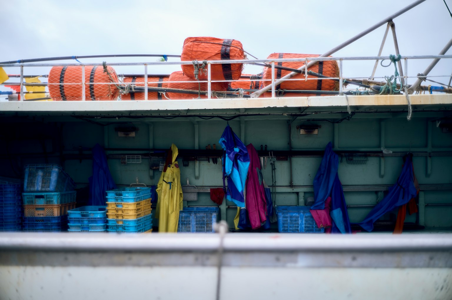 Equipo de pesca colorido y contenedores en la cubierta de un barco con boyas naranjas
