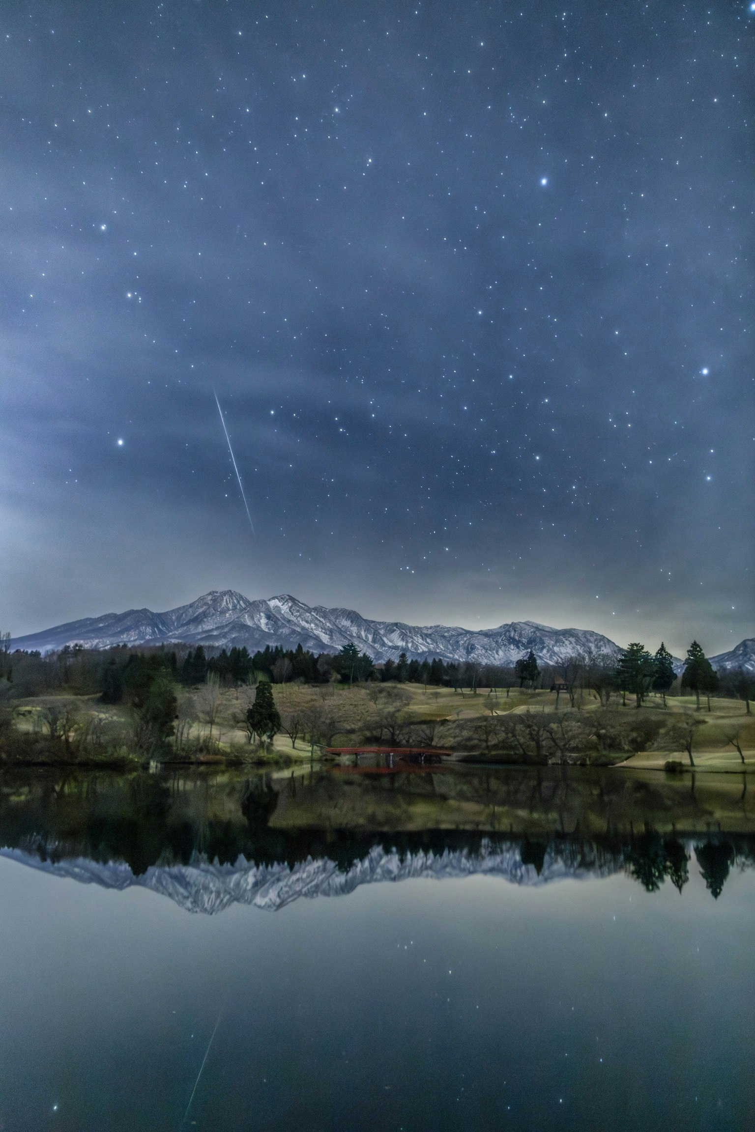 Cielo stellato della pioggia di meteoriti delle Gemelli sopra montagne riflesse in un lago