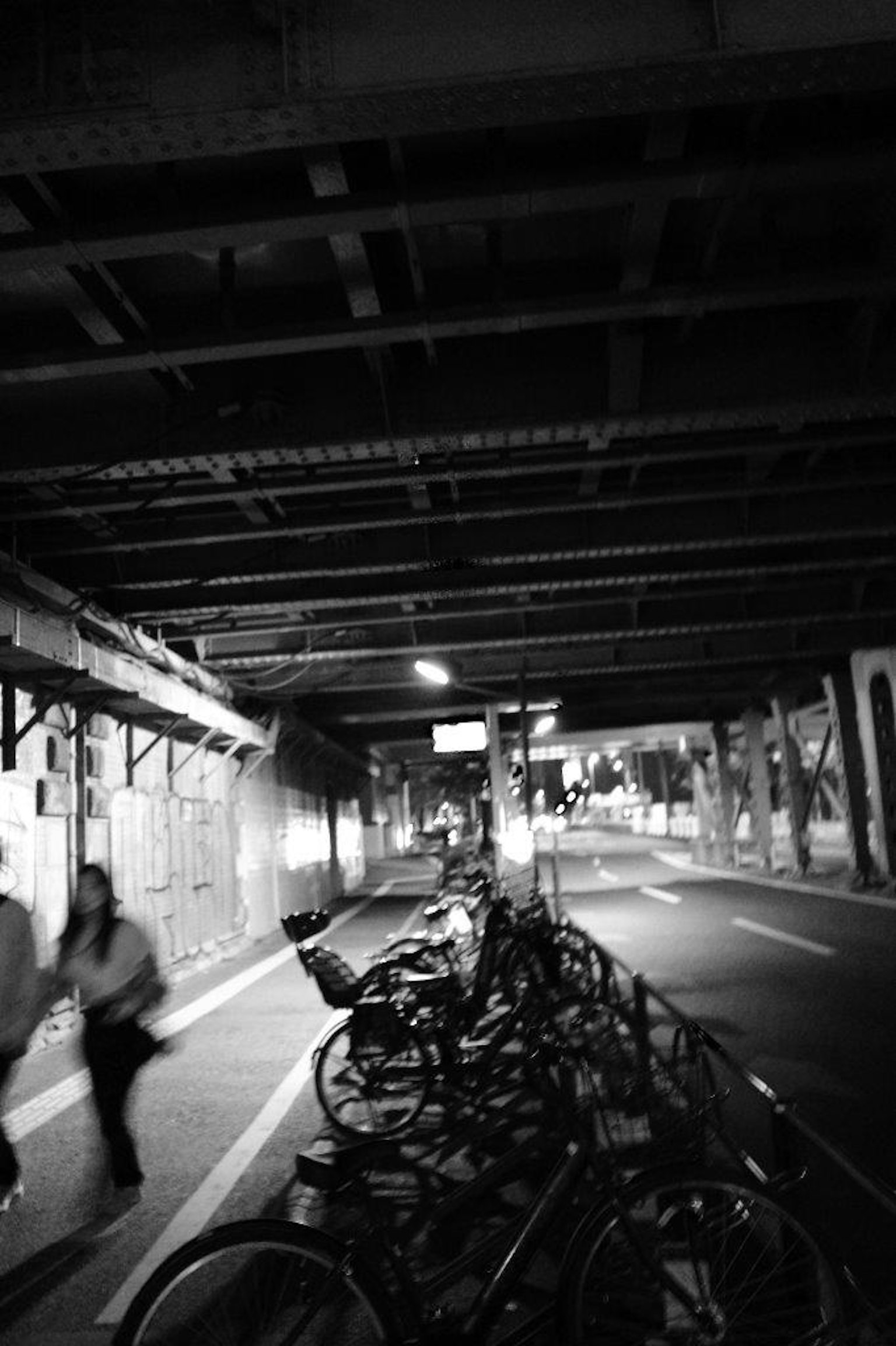 Foto in bianco e nero di biciclette parcheggiate sotto un viadotto con pedoni