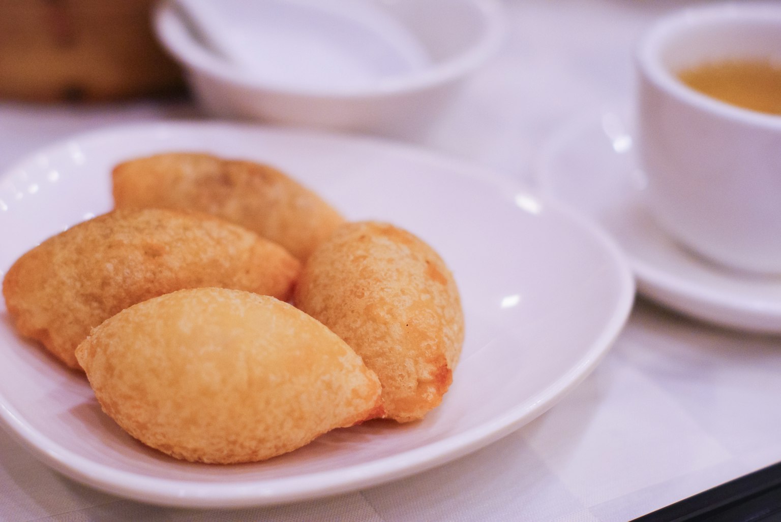 Dumplings fritos dorados en un plato blanco con una taza de té al fondo