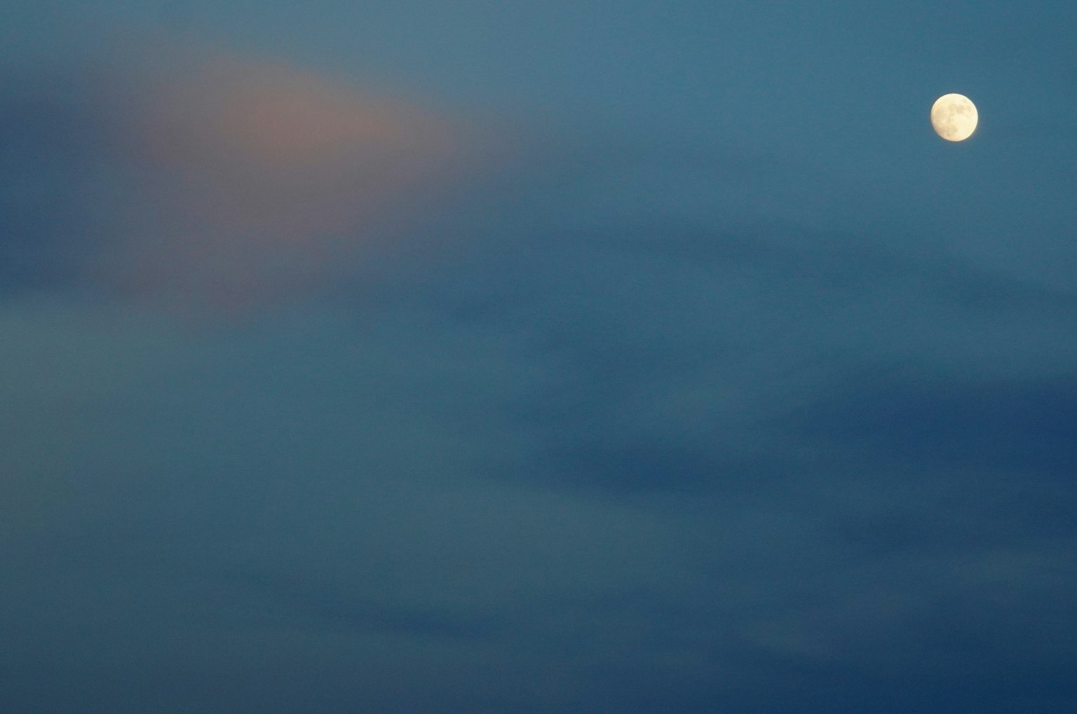 Bright moon in a blue sky with soft clouds