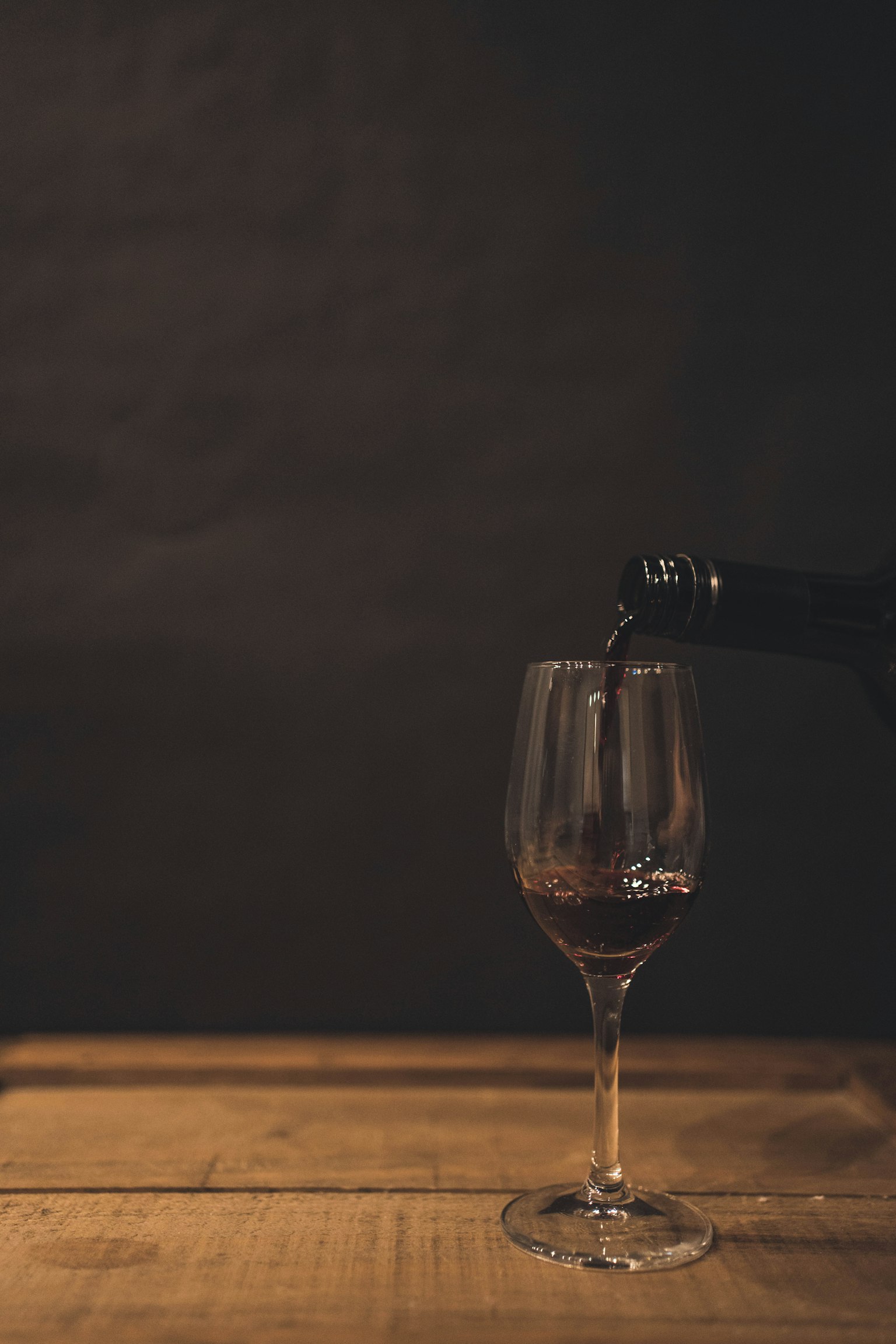 A wine bottle pouring into a glass on a wooden table