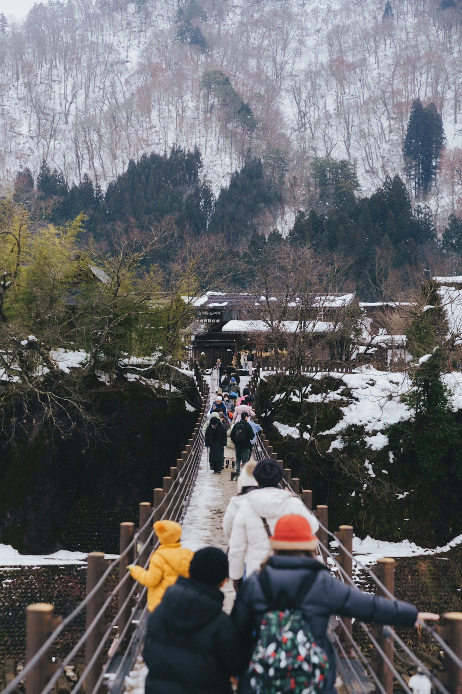人們走在雪覆蓋的橋上，背景是山脈