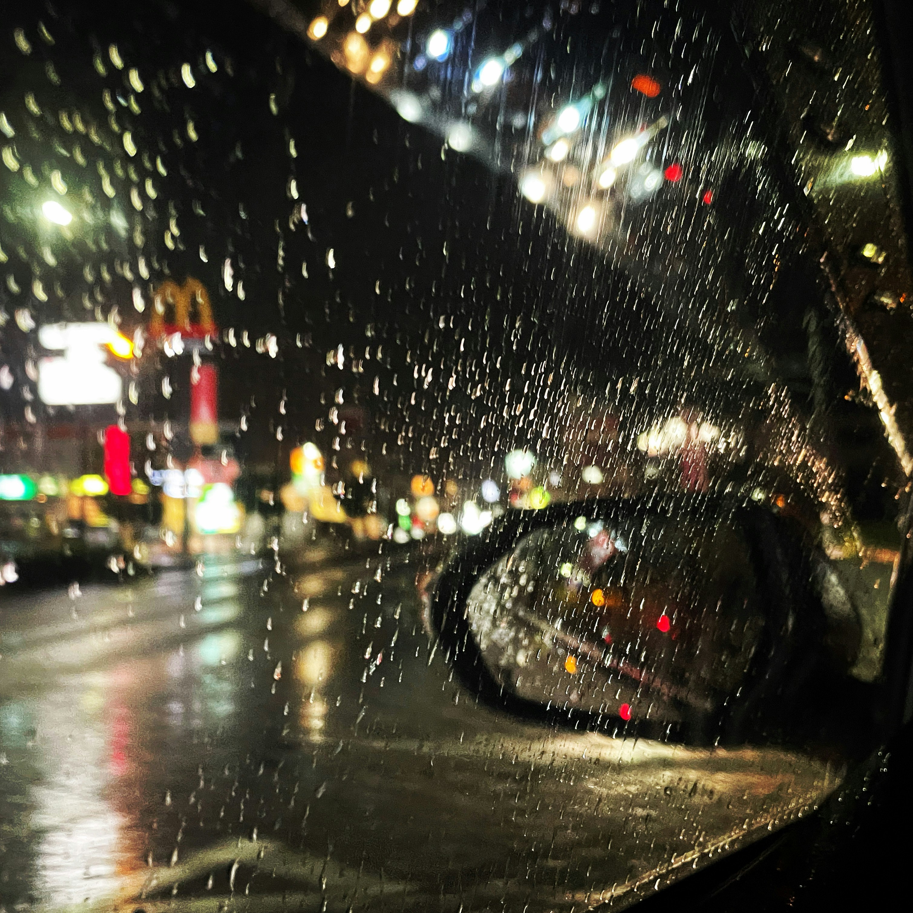 雨粒が降る夜の街路と車のライトがにじむ風景