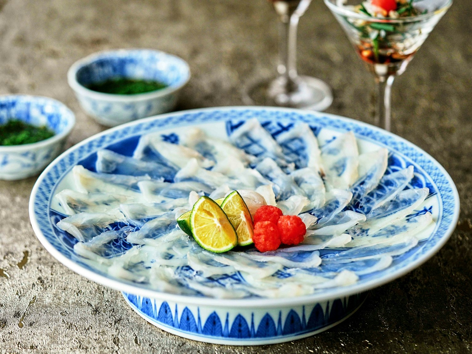 Poisson tranché finement disposé sur une assiette bleue avec du citron vert et des framboises