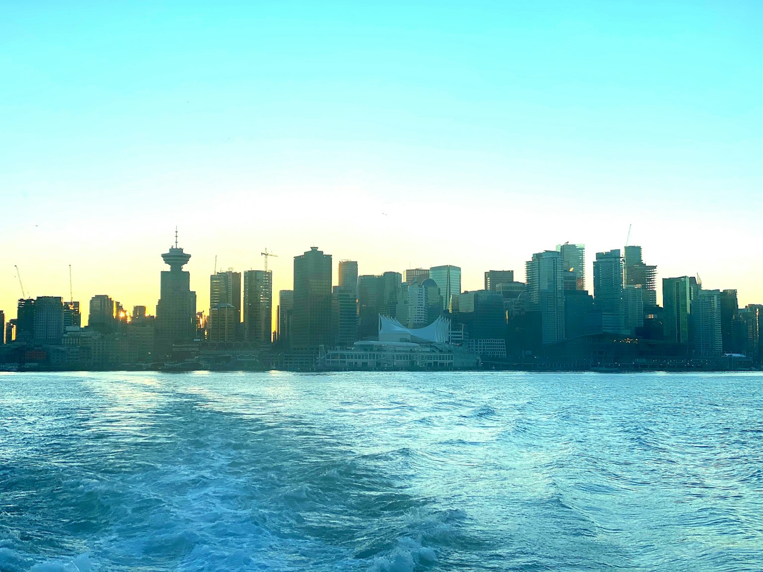 Skyline di Vancouver al tramonto con edifici che si riflettono sull'acqua e cielo blu