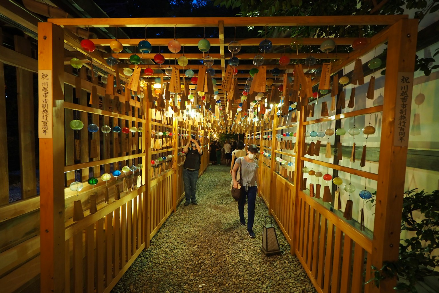 A person walking through a path adorned with wind chimes at night