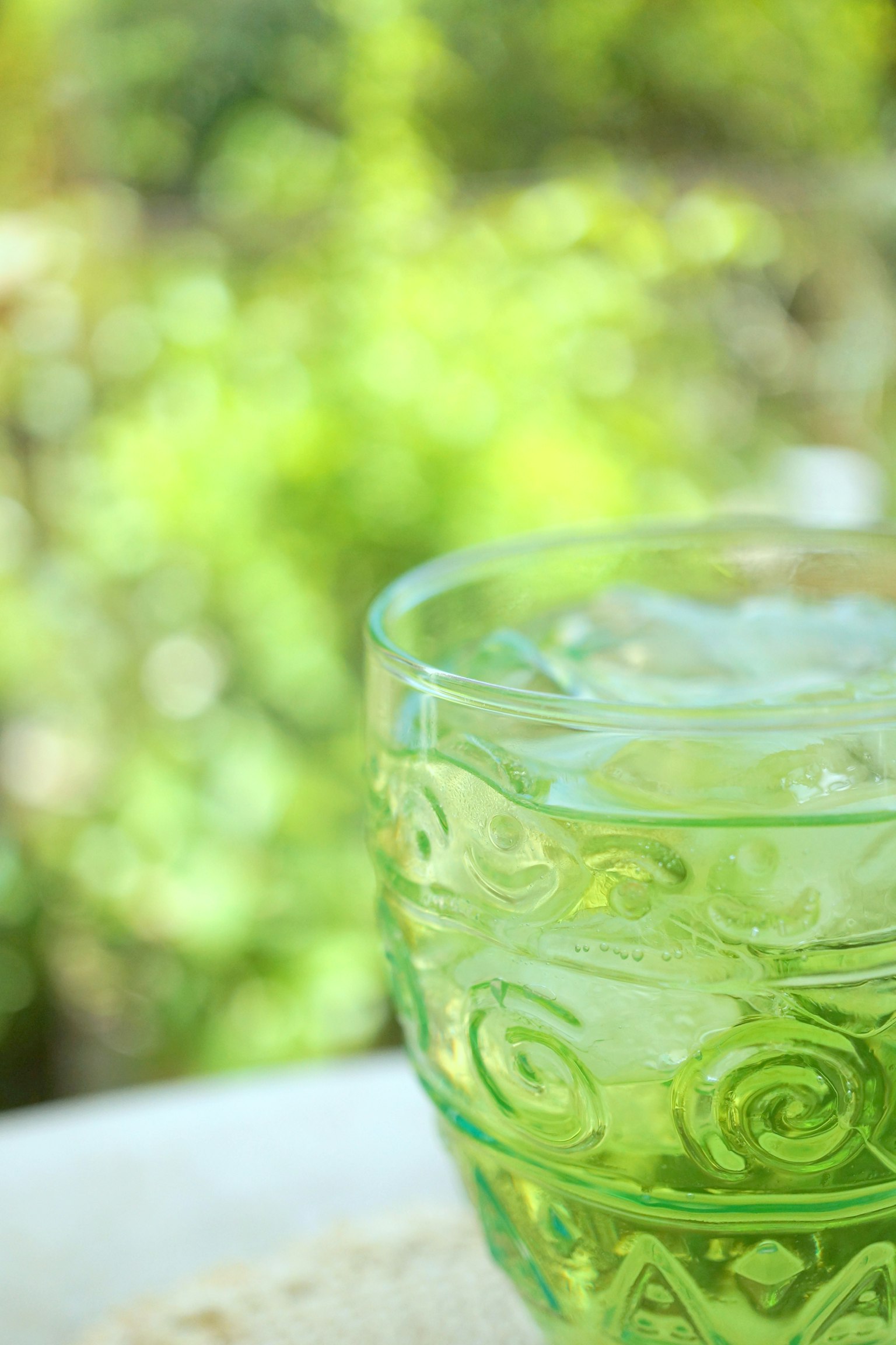 Green glass cup filled with ice against a blurred outdoor background