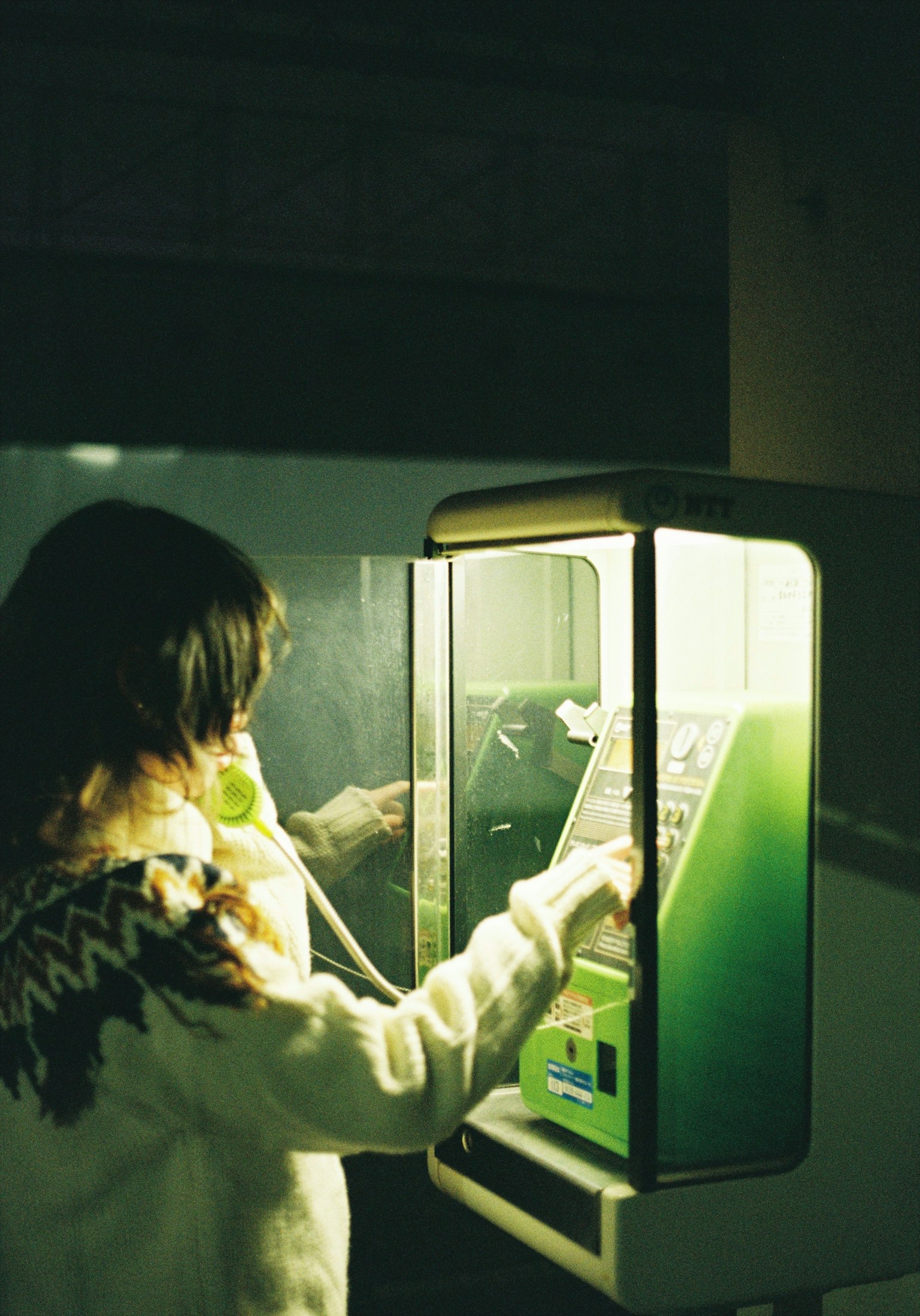 Femme utilisant une cabine téléphonique avec lumière verte, ambiance rétro