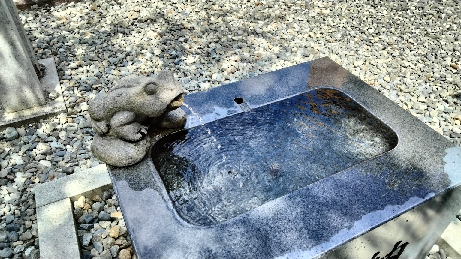 Immagine di una scultura di rana in pietra accanto a una vasca d'acqua