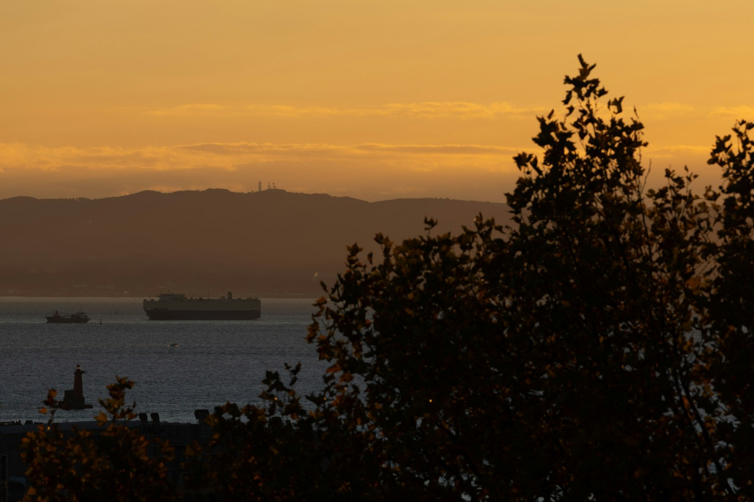 Silueta de barcos en el mar con montañas al atardecer