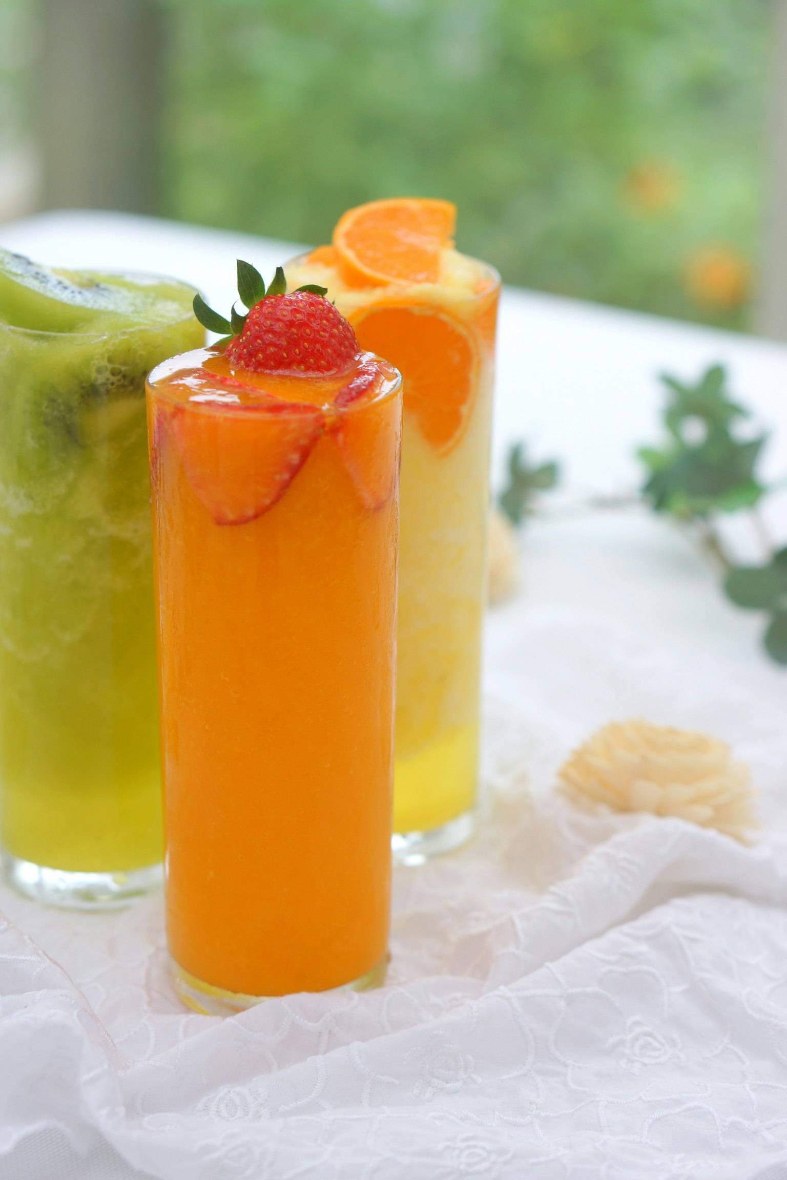 Une boisson orange vif garnie d'une fraise au centre avec des plantes vertes en arrière-plan
