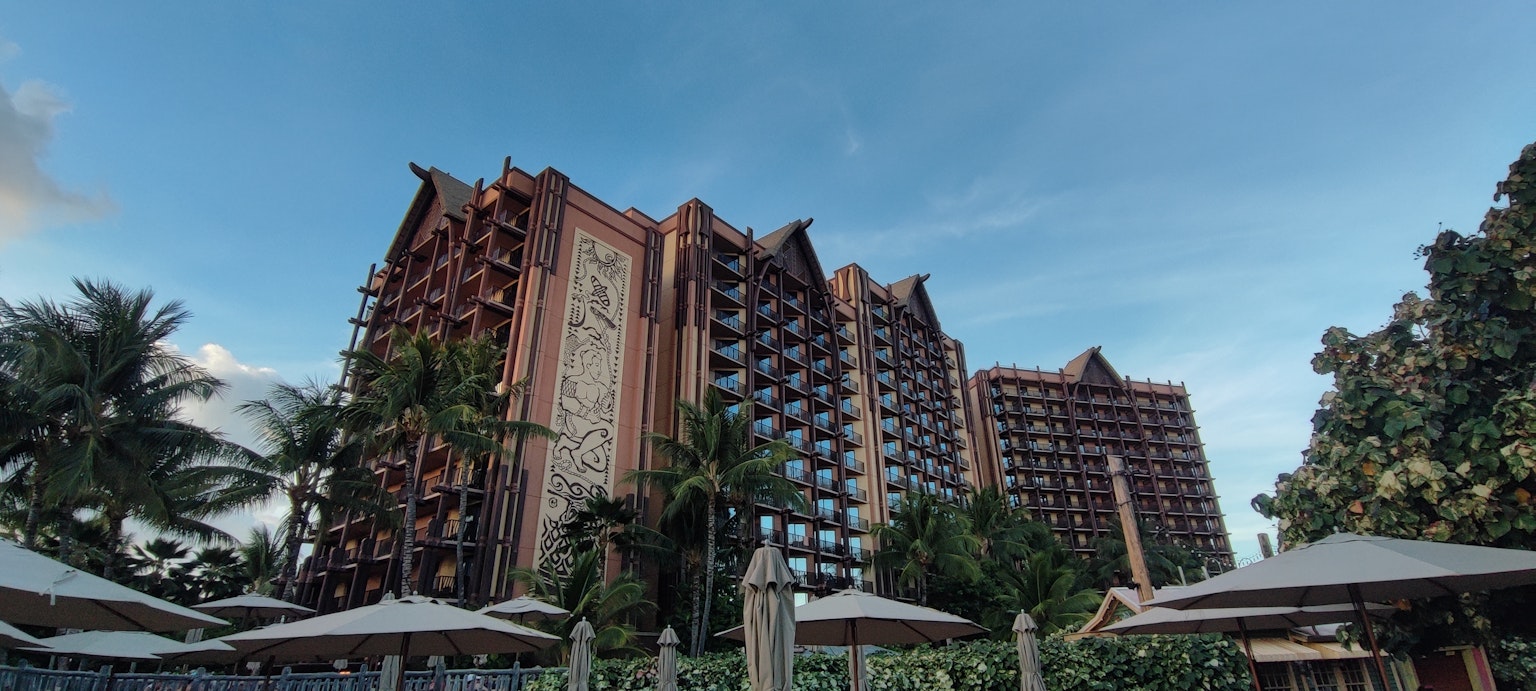 Außenansicht eines Resorthotels mit blauem Himmel Palmen und Sonnenschirmen