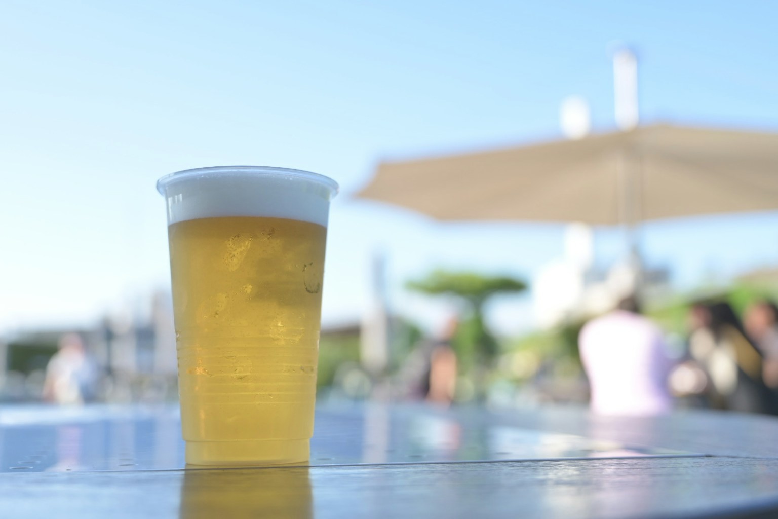 ビールが入った透明なカップがテーブルの上に置かれ青い空が背景にある