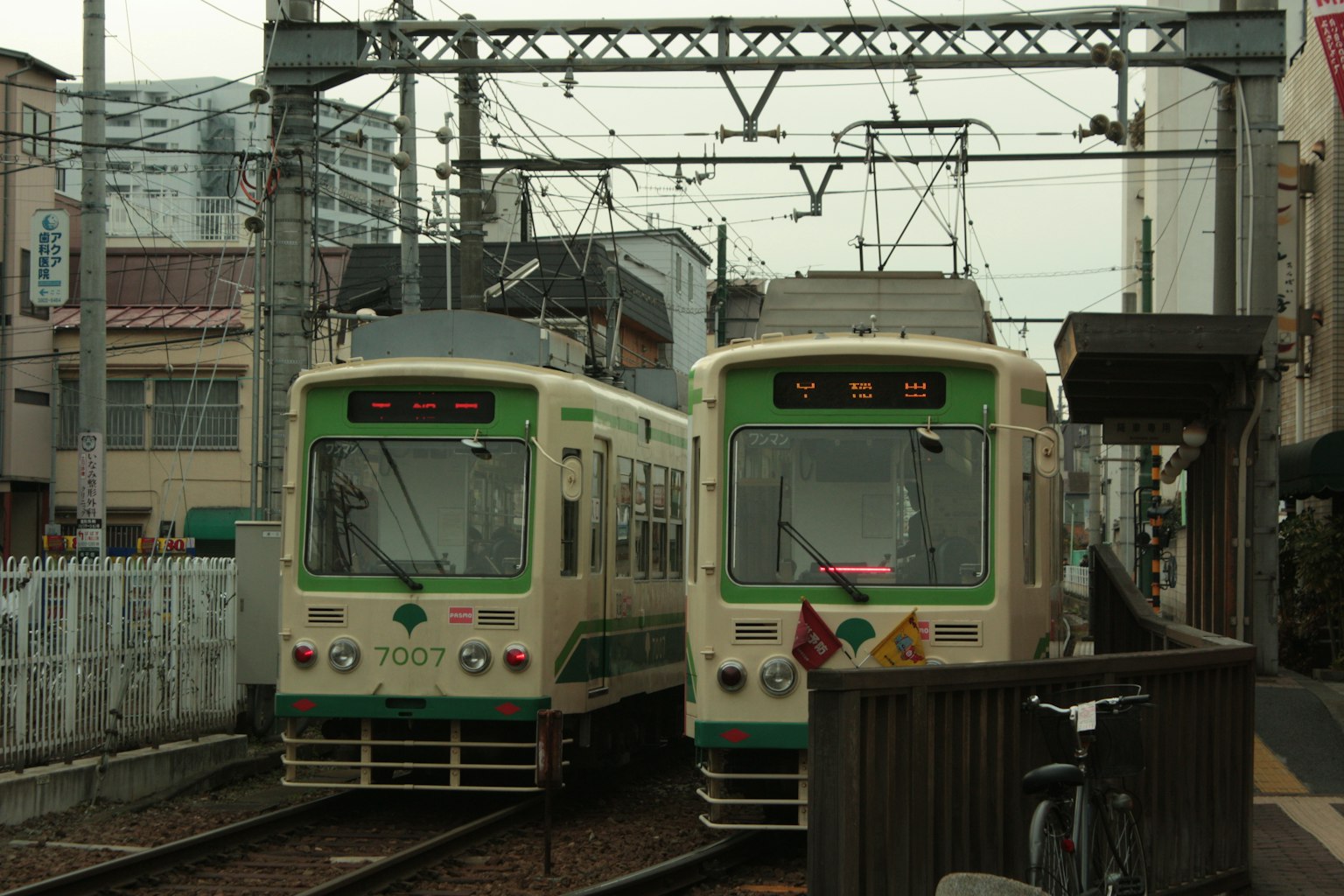 Deux tramways stationnés à une gare avec des lignes aériennes et des bâtiments urbains en arrière-plan