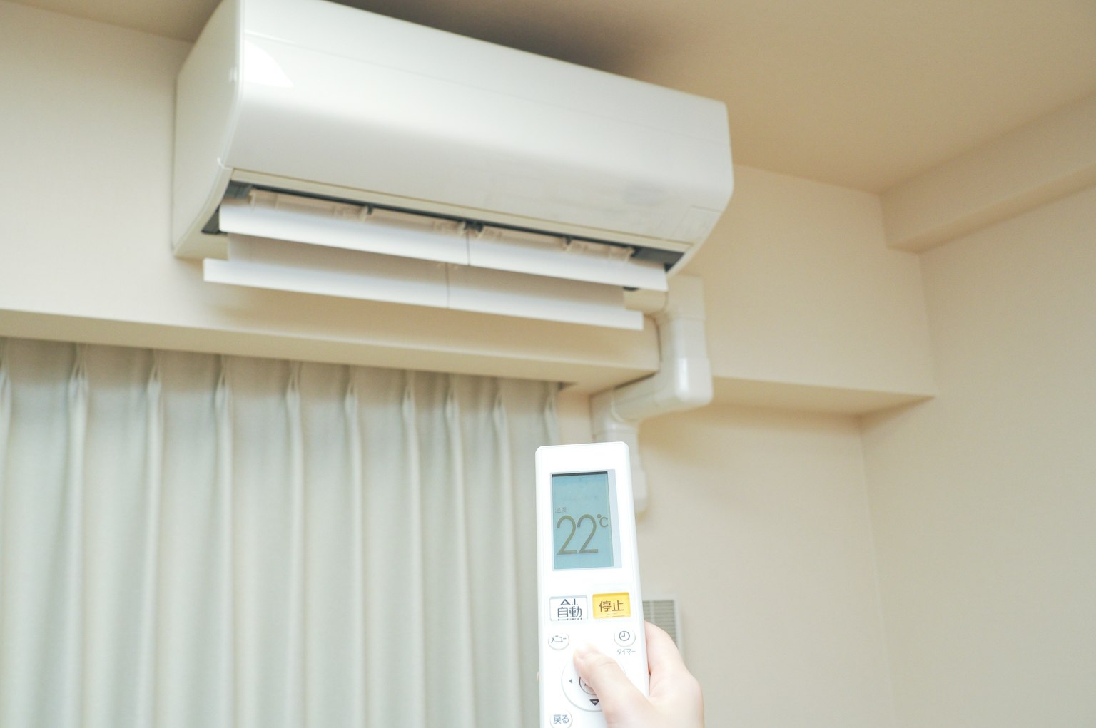 Une main tenant une télécommande de climatiseur avec un climatiseur mural