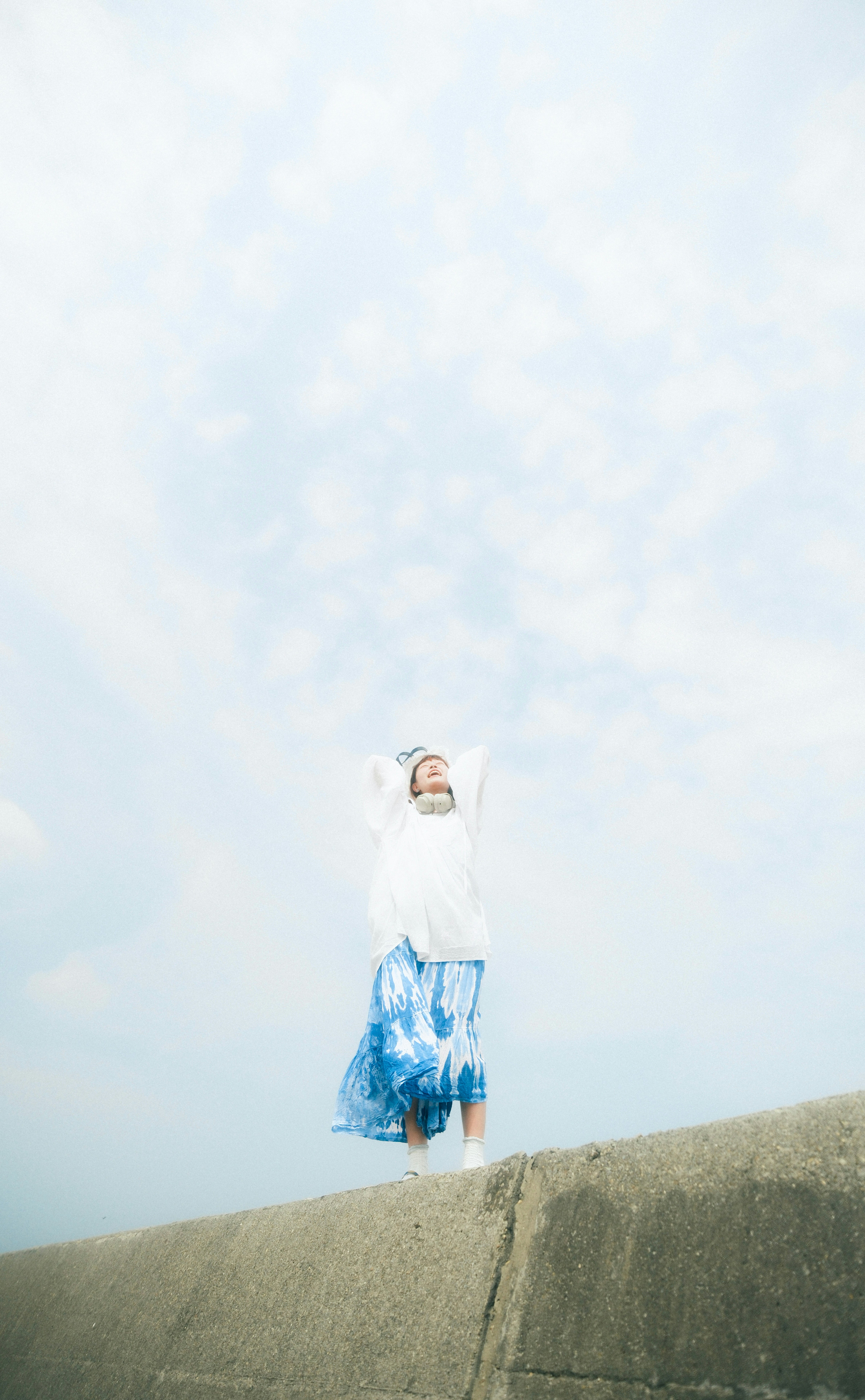 青空の下で白い服のモデルが丘の上に立つ