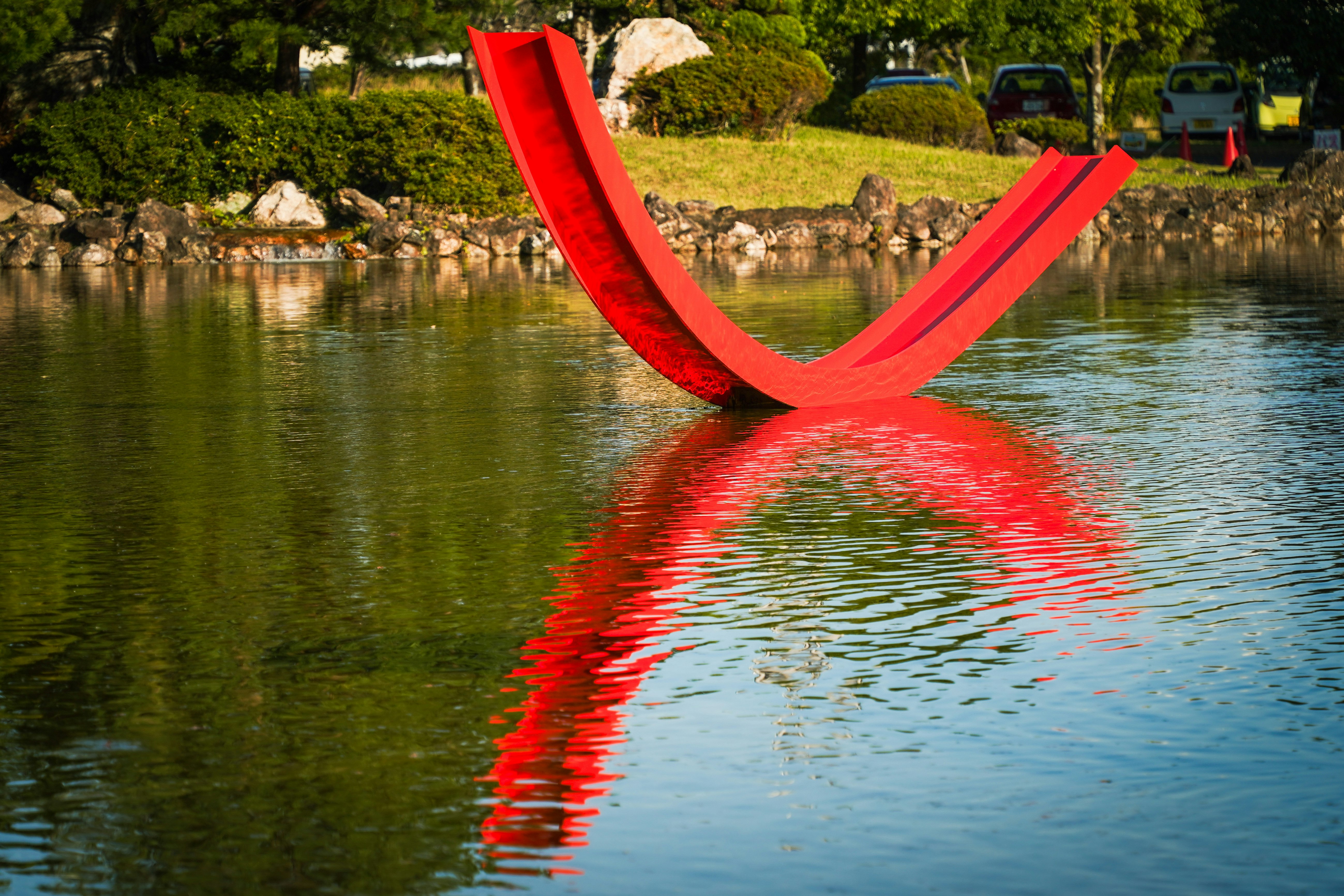 sculpture en forme de ruban rouge reflétée sur un étang de jardin