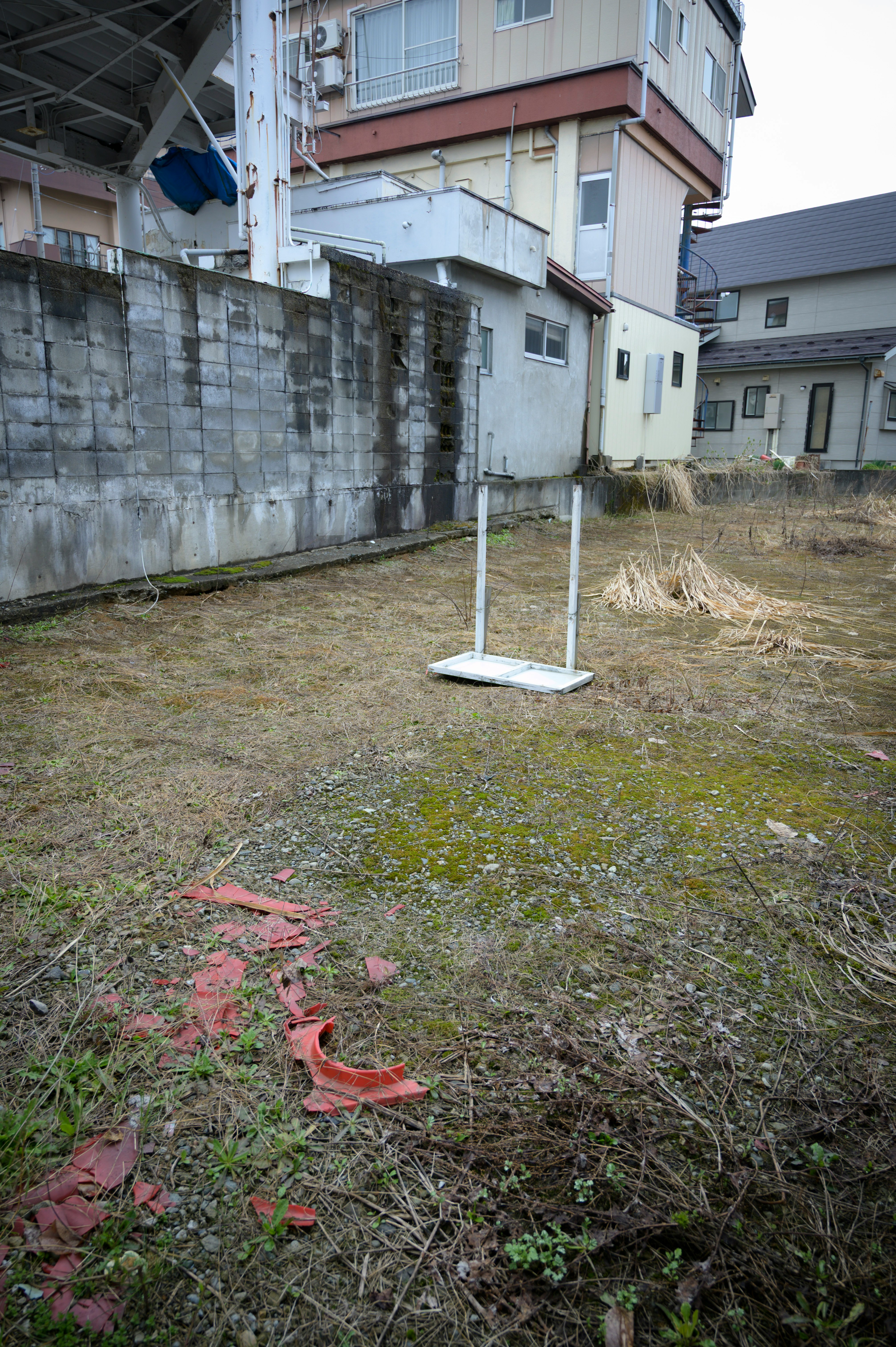 空地の雑草とフェンス支柱のある住宅裏の敷地